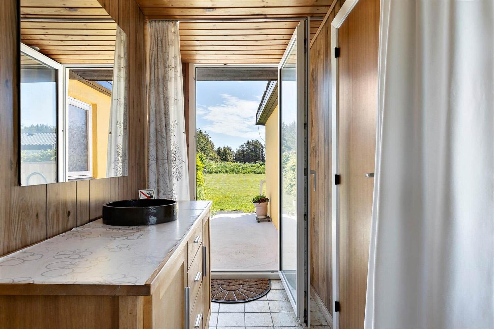 Bathroom with wooden walls, sink, and view onto the terrace.
