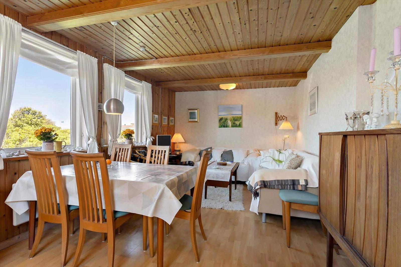 Dining room with table and chairs. Living area with sofa and coffee table. Wooden ceiling and windows with view.