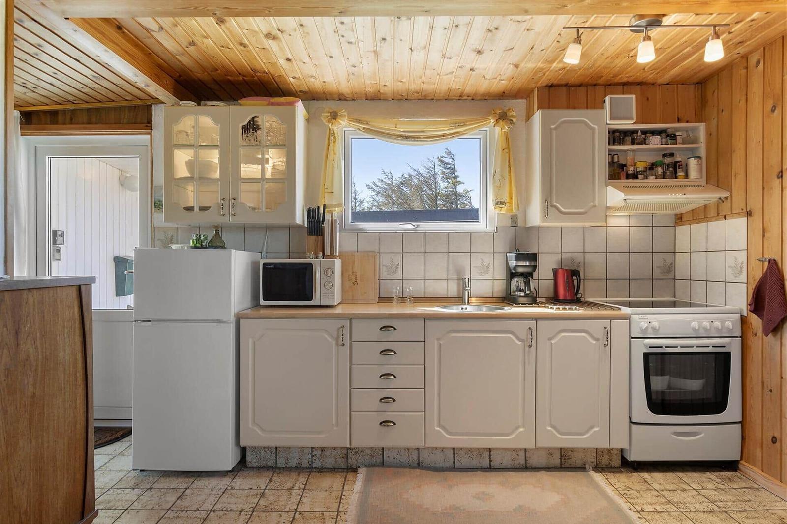 Kitchen with white cabinets, refrigerator, stove, and window with view of trees.
