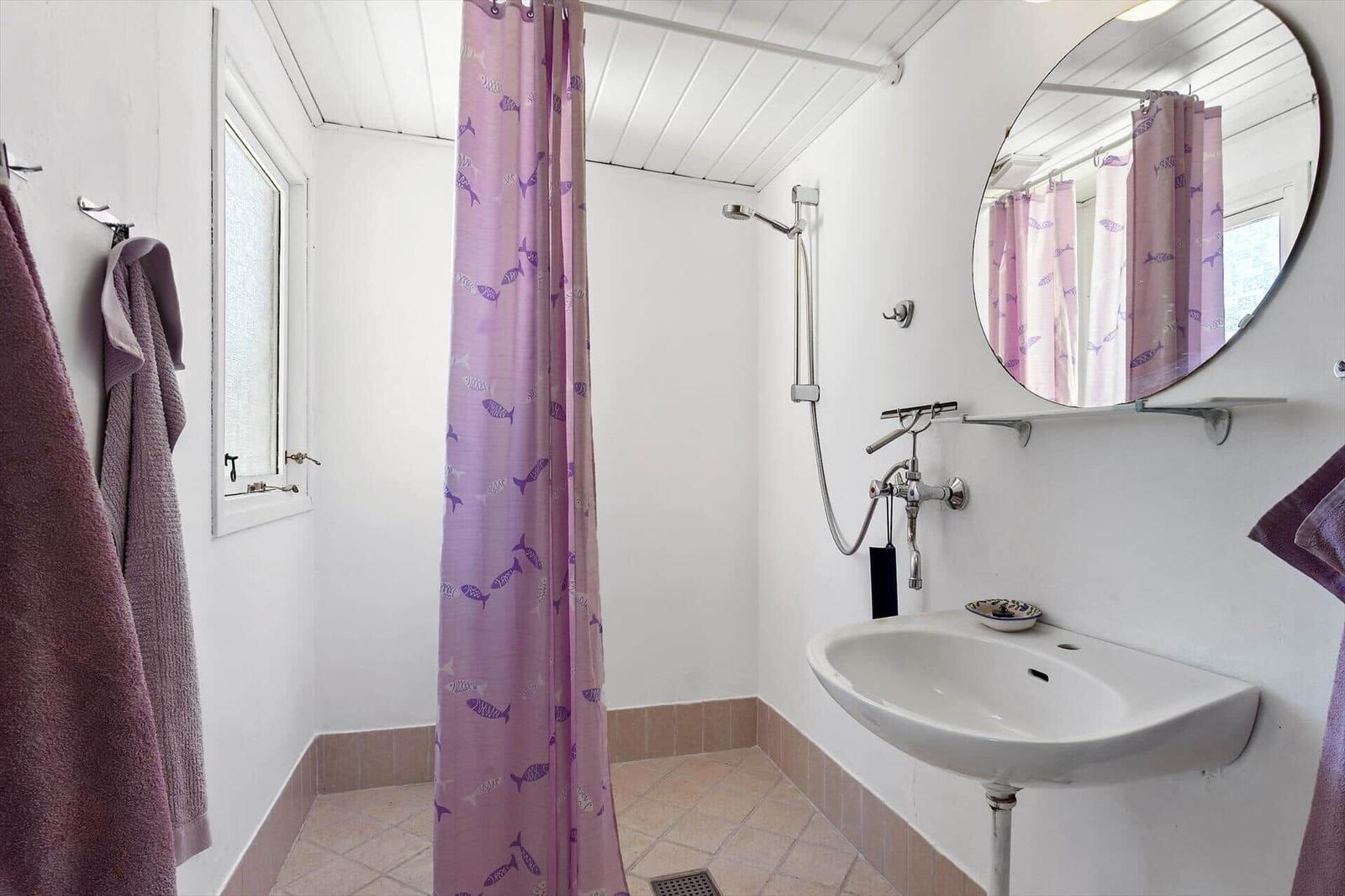 Bathroom with shower, sink, and mirror. Shower curtain with fish pattern.