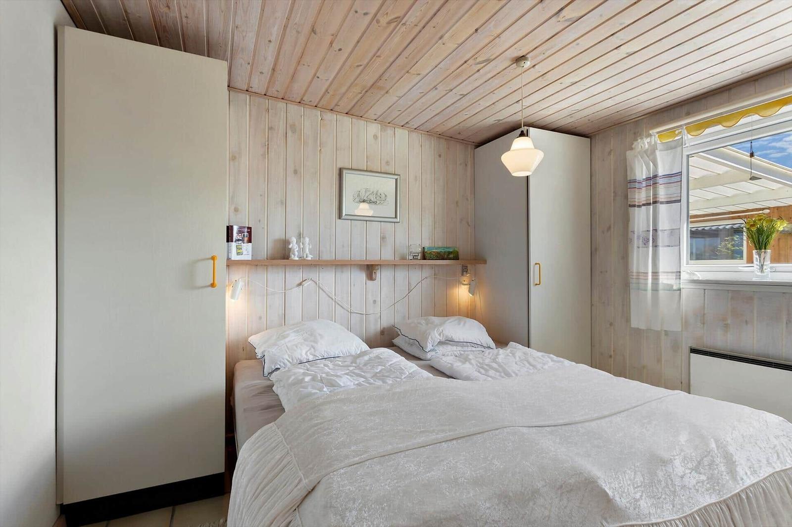 Bedroom with wooden walls, bed, wardrobe, and window with view.