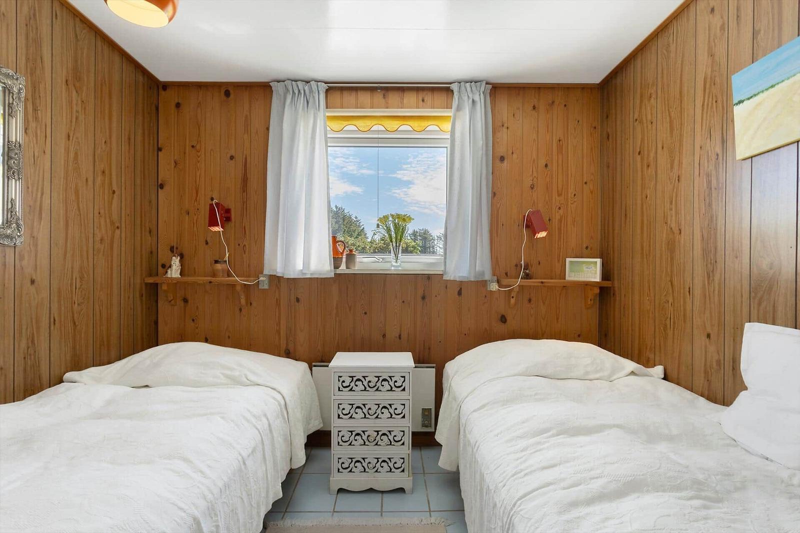 Two beds with white sheets, wooden walls, window with view outside, and nightstand.