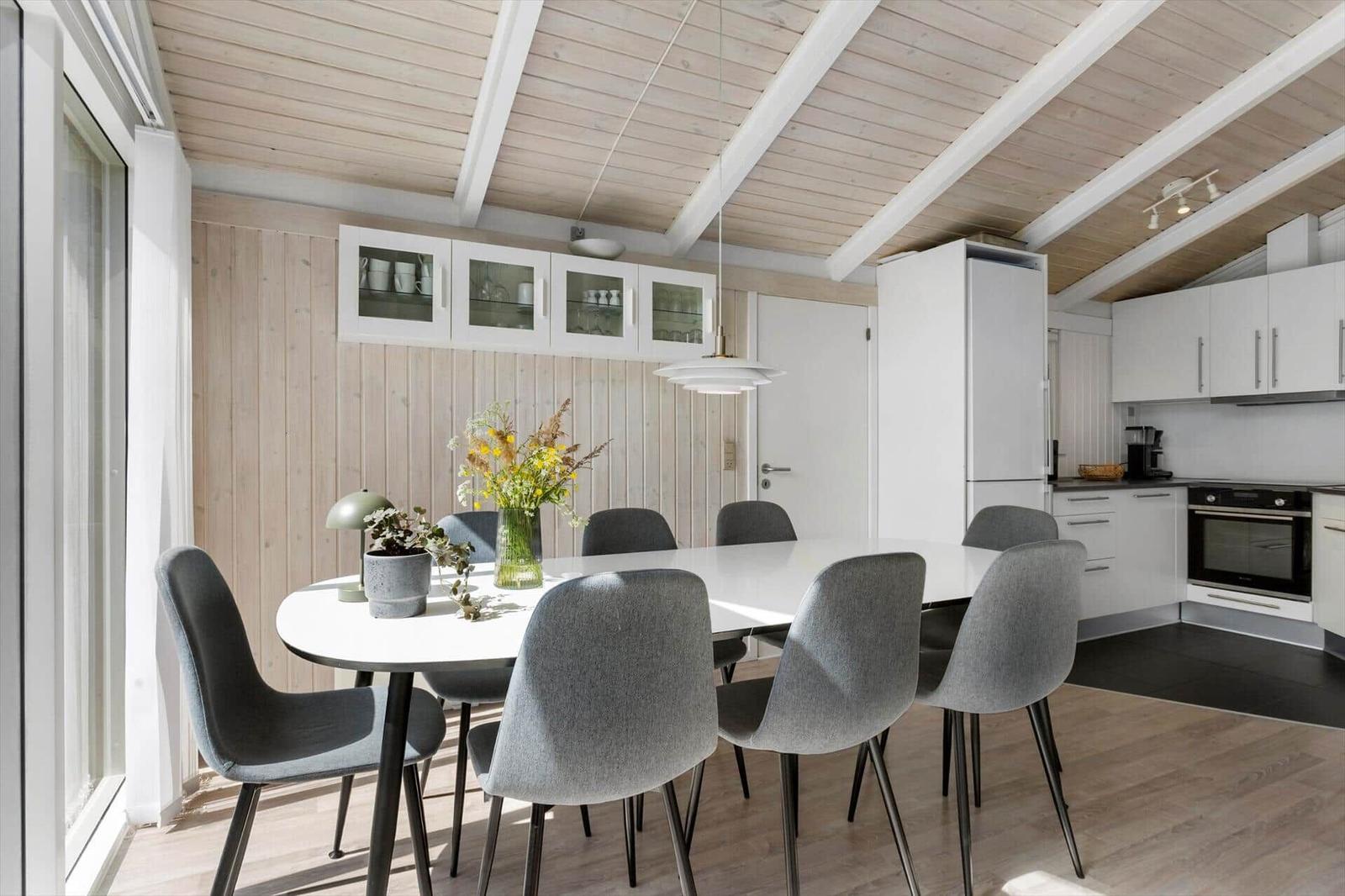 Dining area with white table, gray chairs, and kitchen with white cabinets.