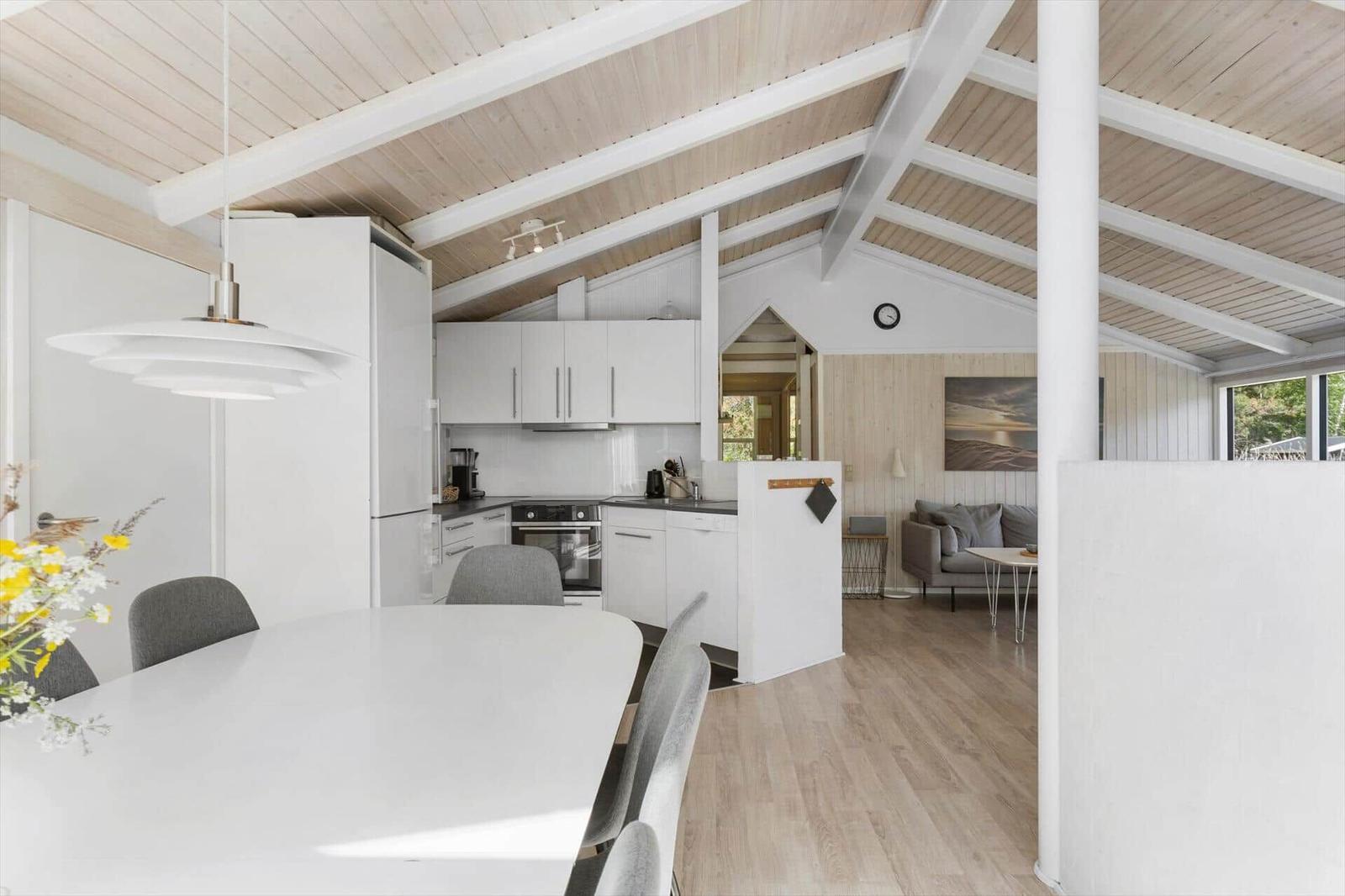Kitchen with dining area and living room in background. Wooden ceiling and light interior.