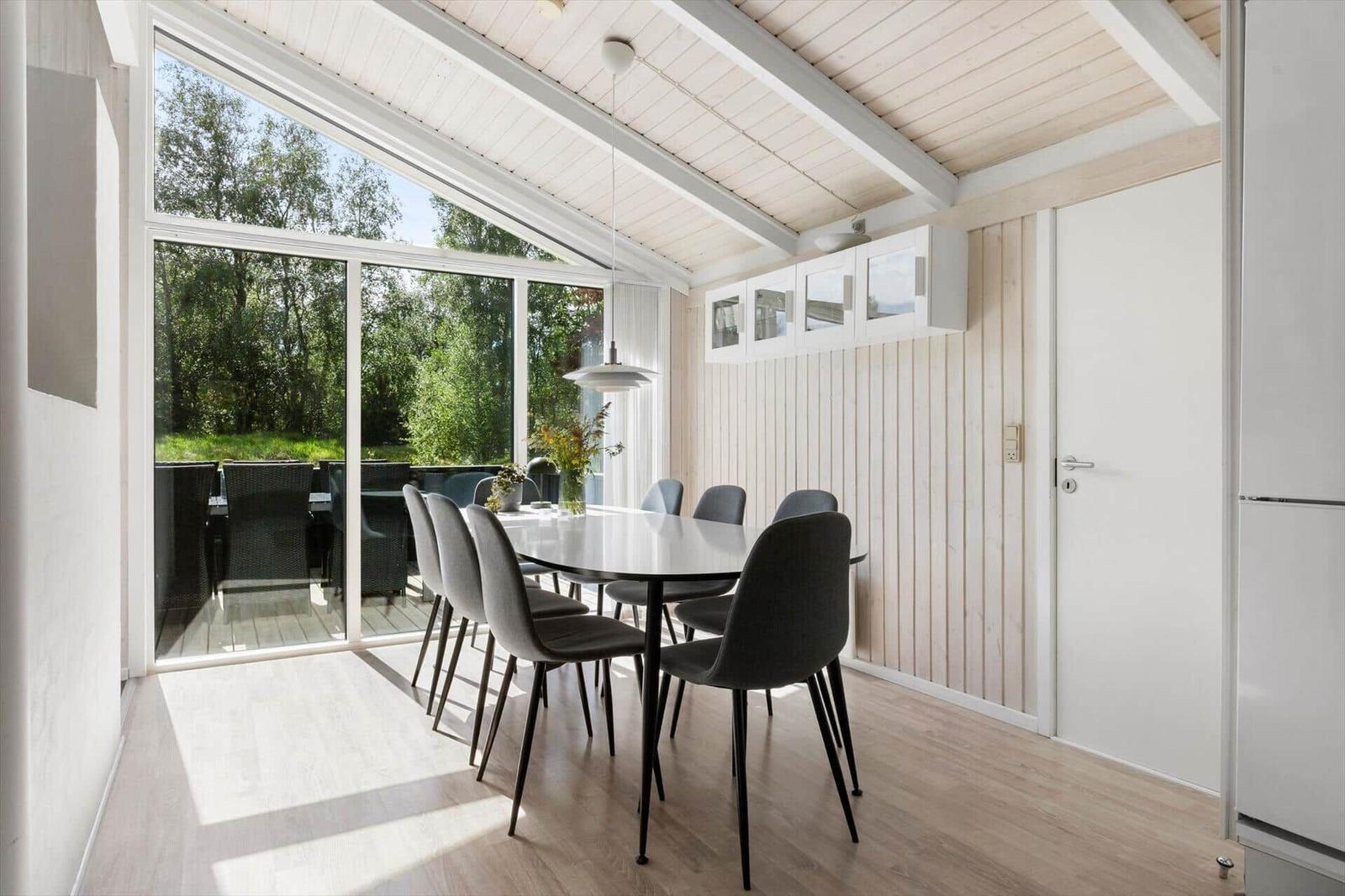 Dining area with table and chairs, large window to terrace, wood wall and white ceiling.