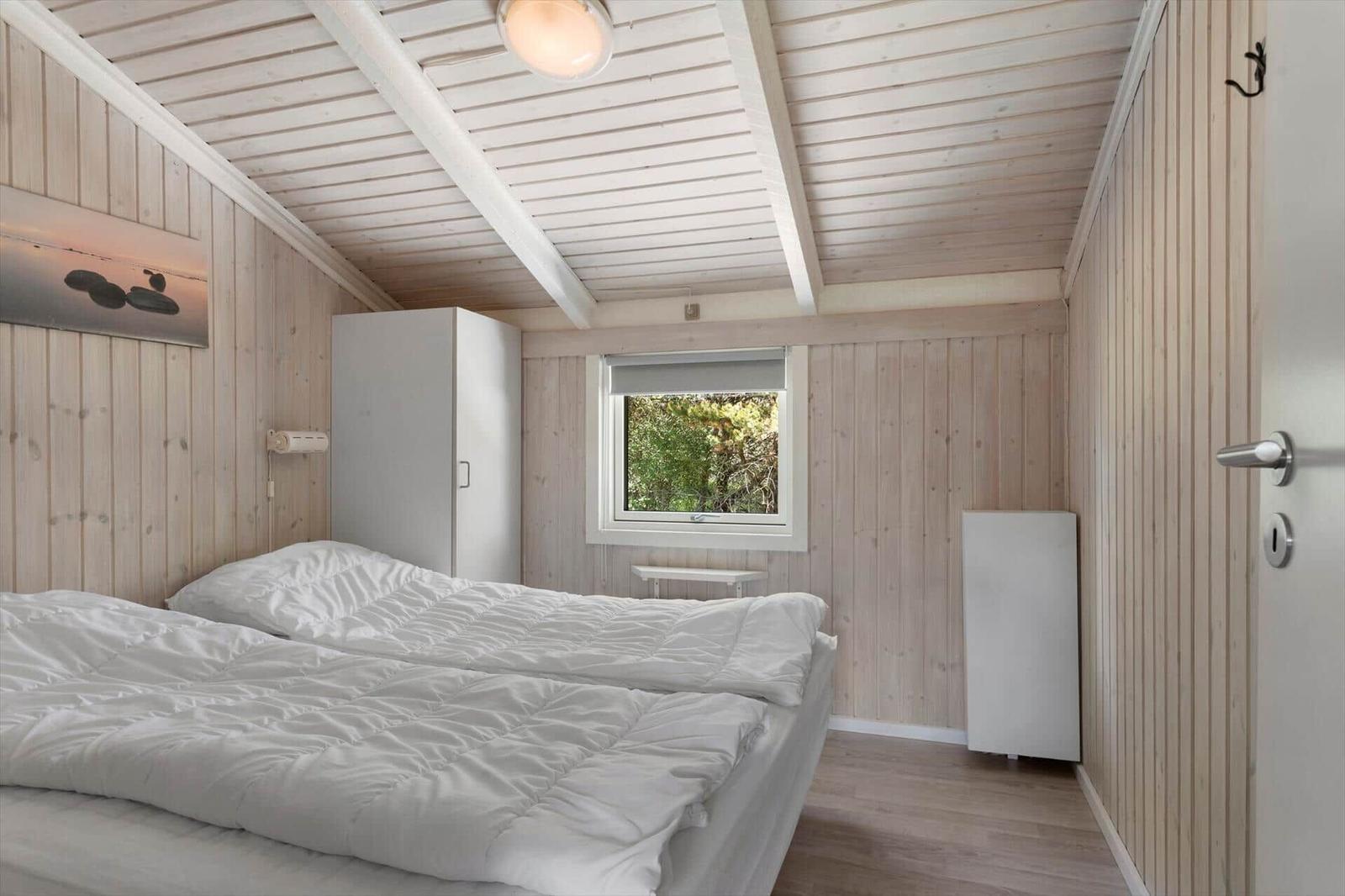 Bedroom with wooden paneling, bed, and window to greenery.