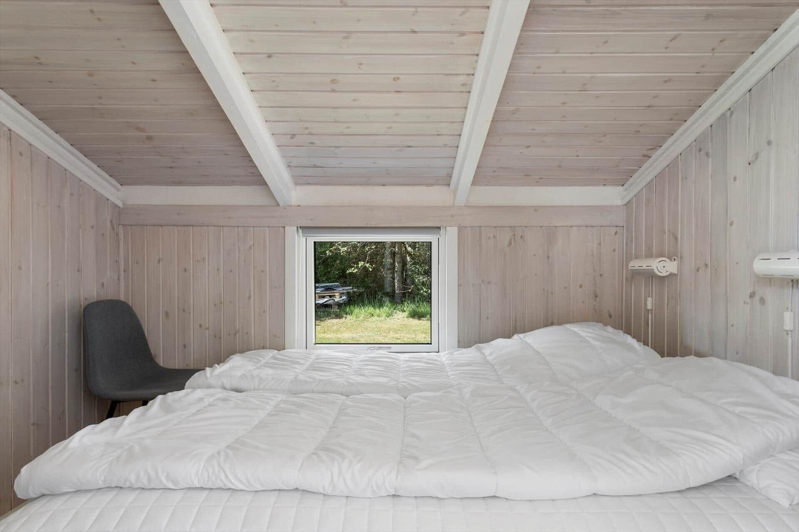Bedroom with bed, window, and chair. Wooden walls and ceiling.