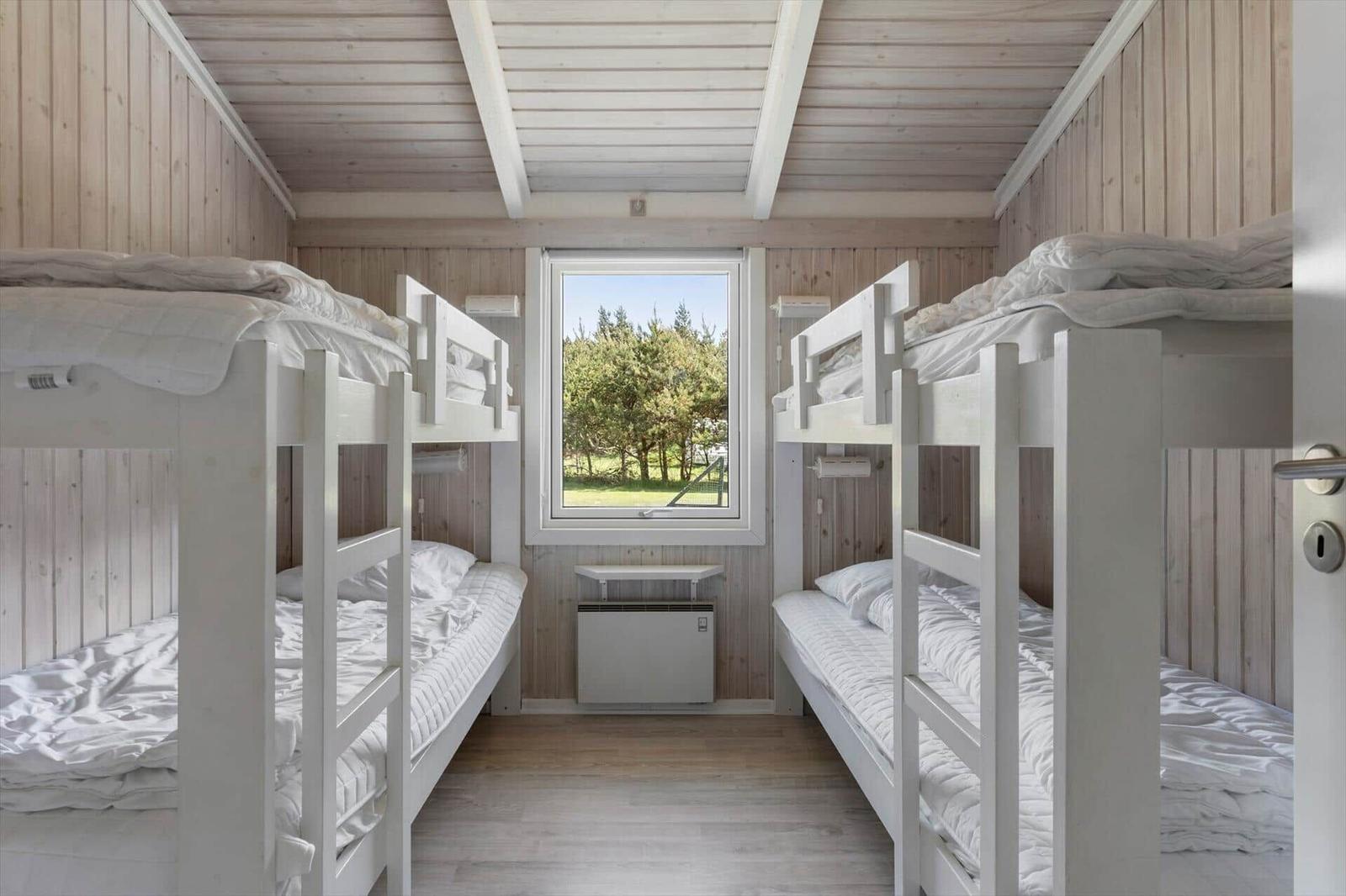 Room with two bunk beds, wooden walls, and window view of green area.