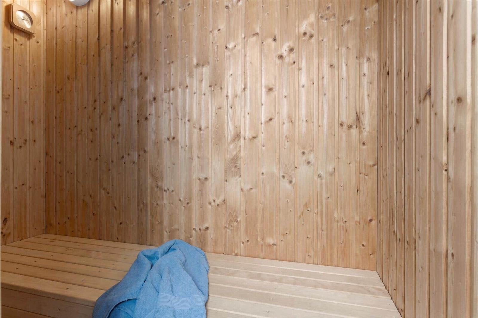 Sauna with wooden walls and bench, blue towel, and wall clock