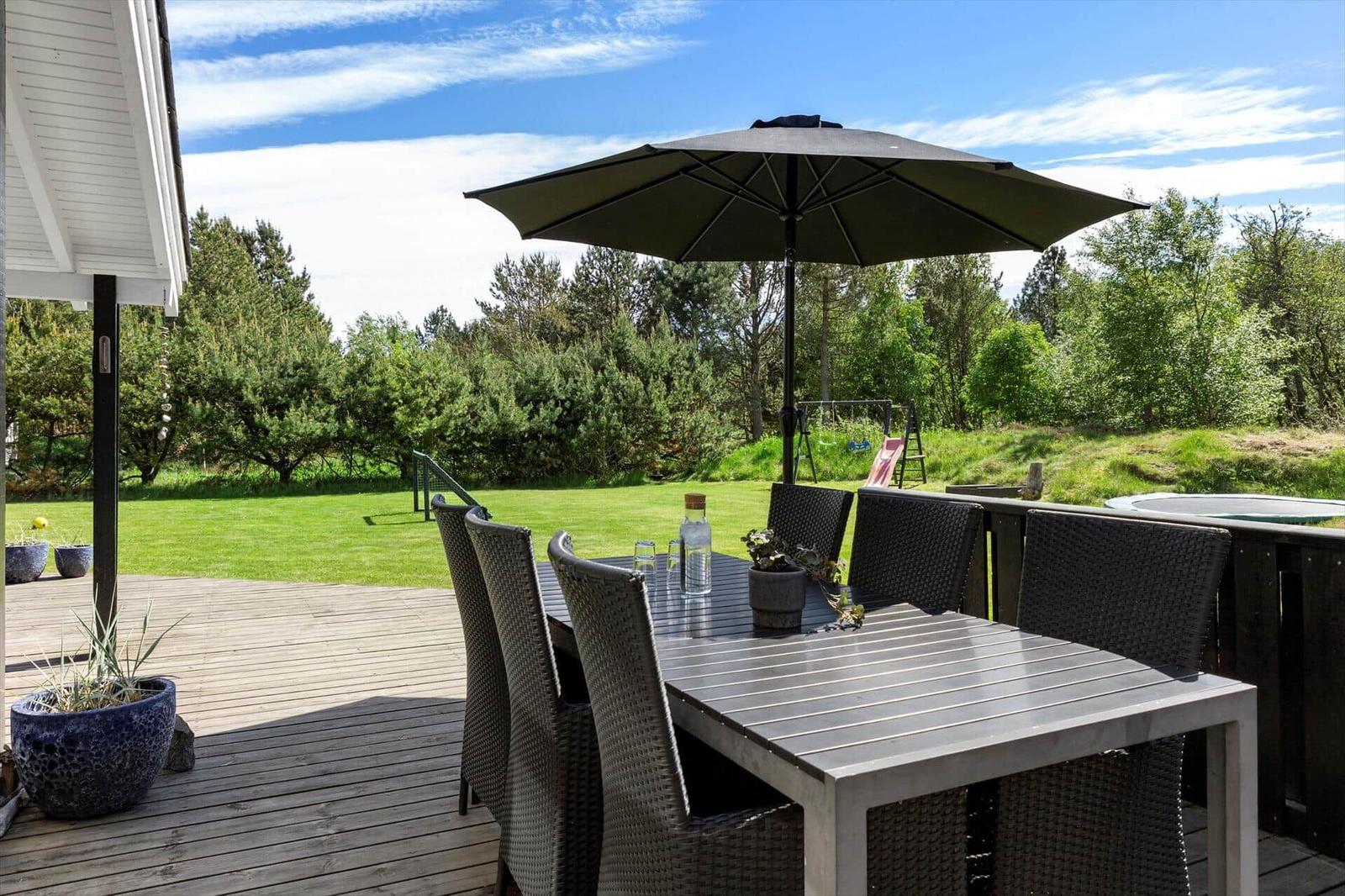 Deck with table, chairs, and umbrella. Lawn and forest in background.