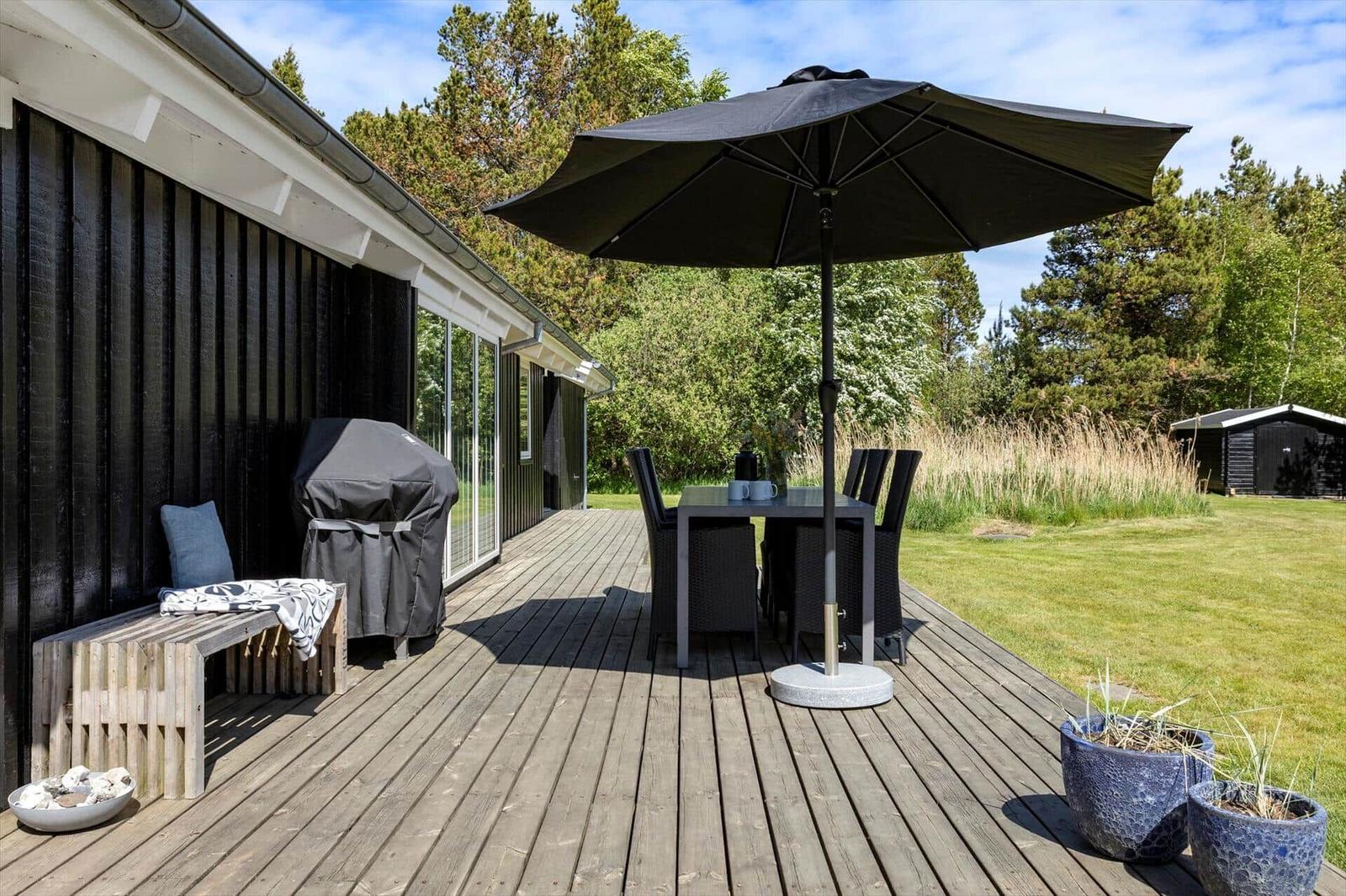 Deck with table, chairs, and umbrella. Grill and bench beside house wall.