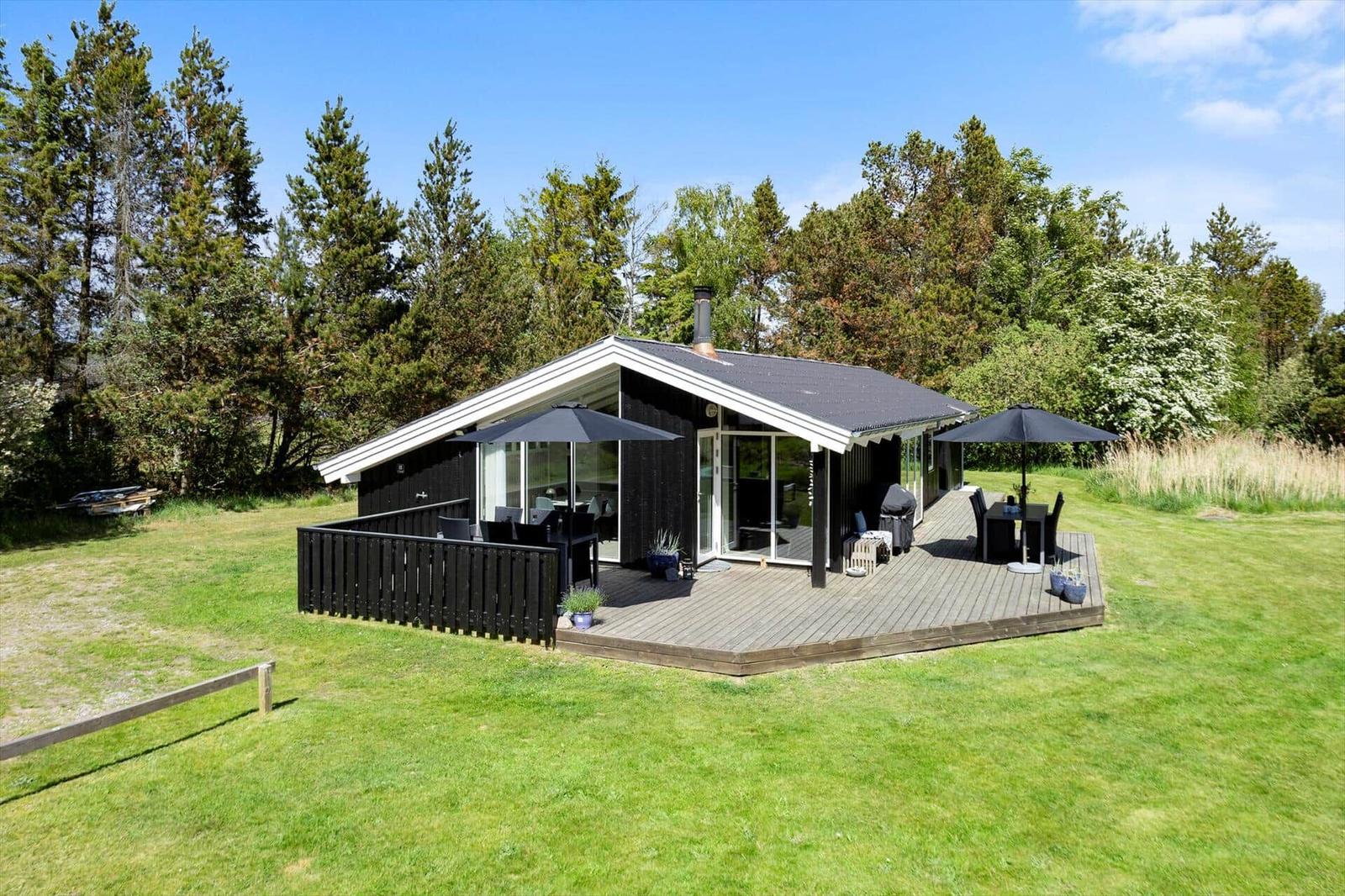 Modern wooden cabin with large deck, grill, and seating areas in the green.