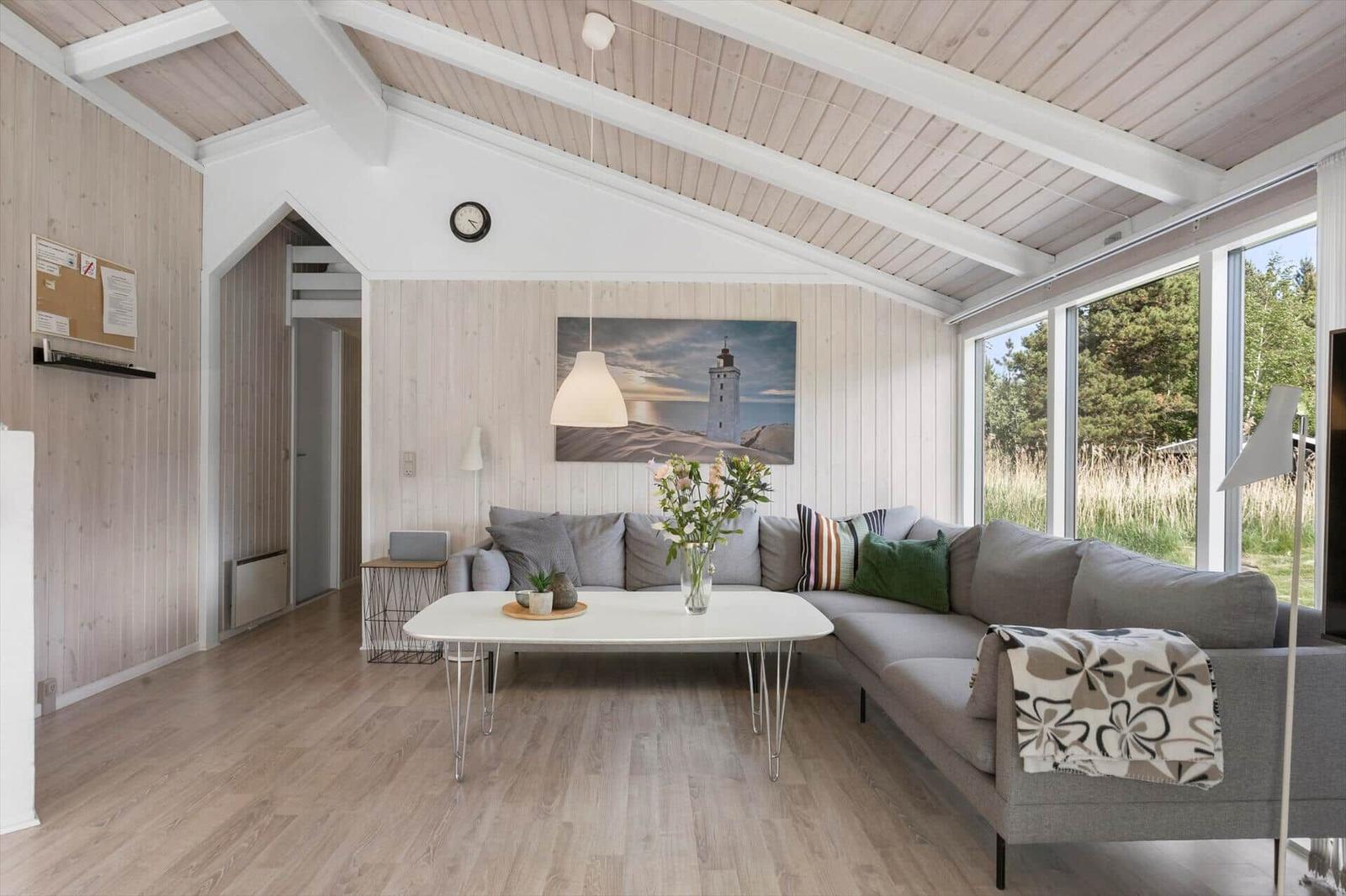 Living room with sofa, table, and large windows. Wooden walls and ceiling.