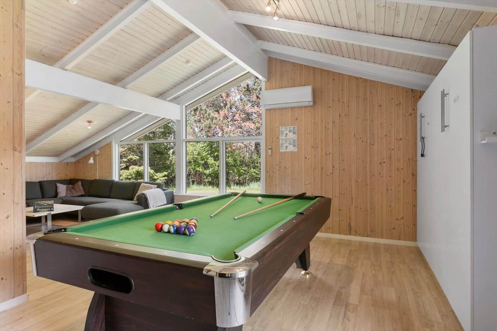 Pool table with balls and cue in a room with wooden wall and large window.