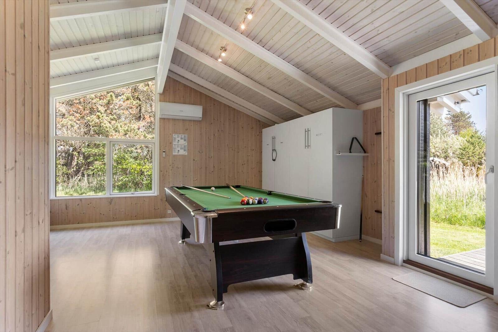 Room with pool table, wooden walls, and windows to nature.