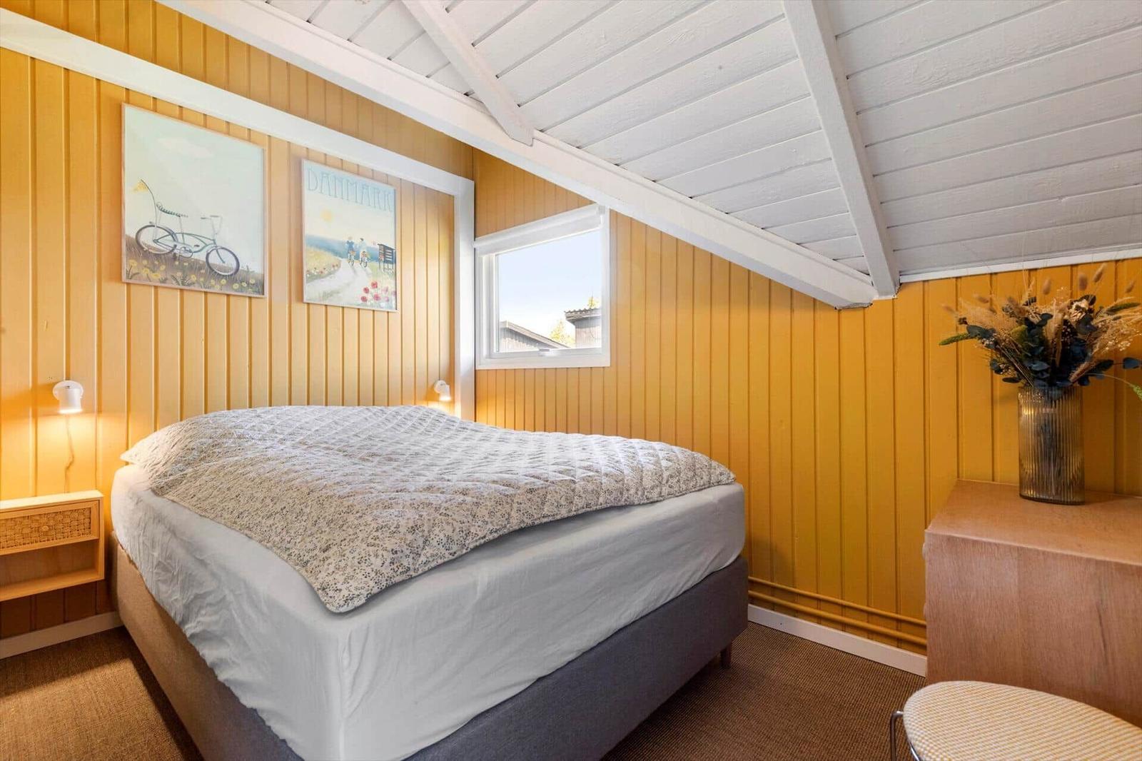 Bedroom with bed, wall art, and window. Wooden walls and white ceiling beams.
