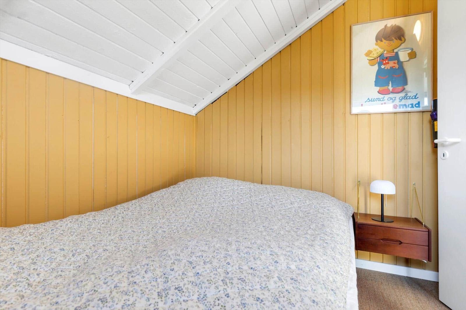 Bedroom with yellow panel wall, bed, and nightstand with lamp.