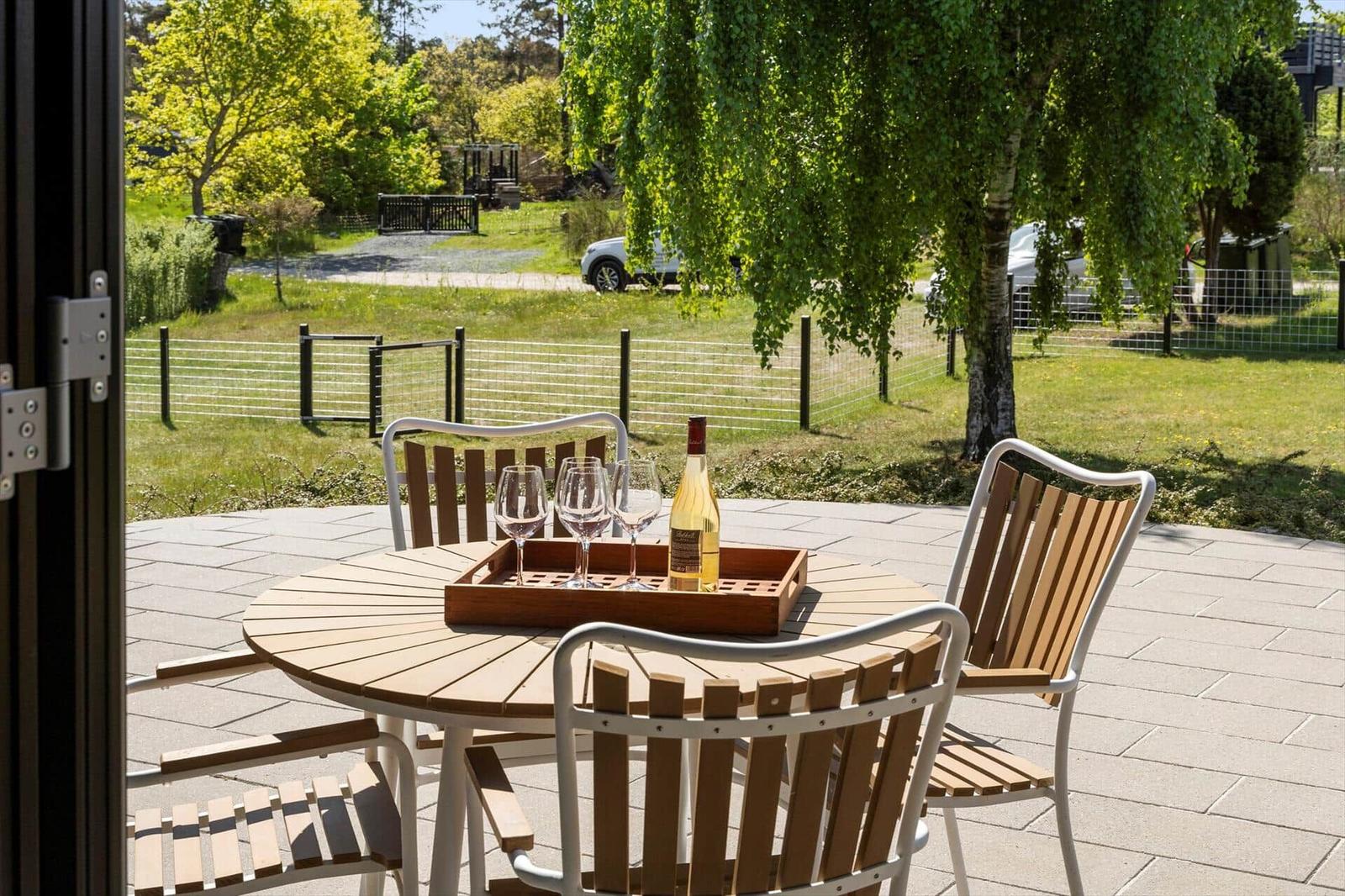 Round table with chairs and wine on terrace overlooking green area and trees.