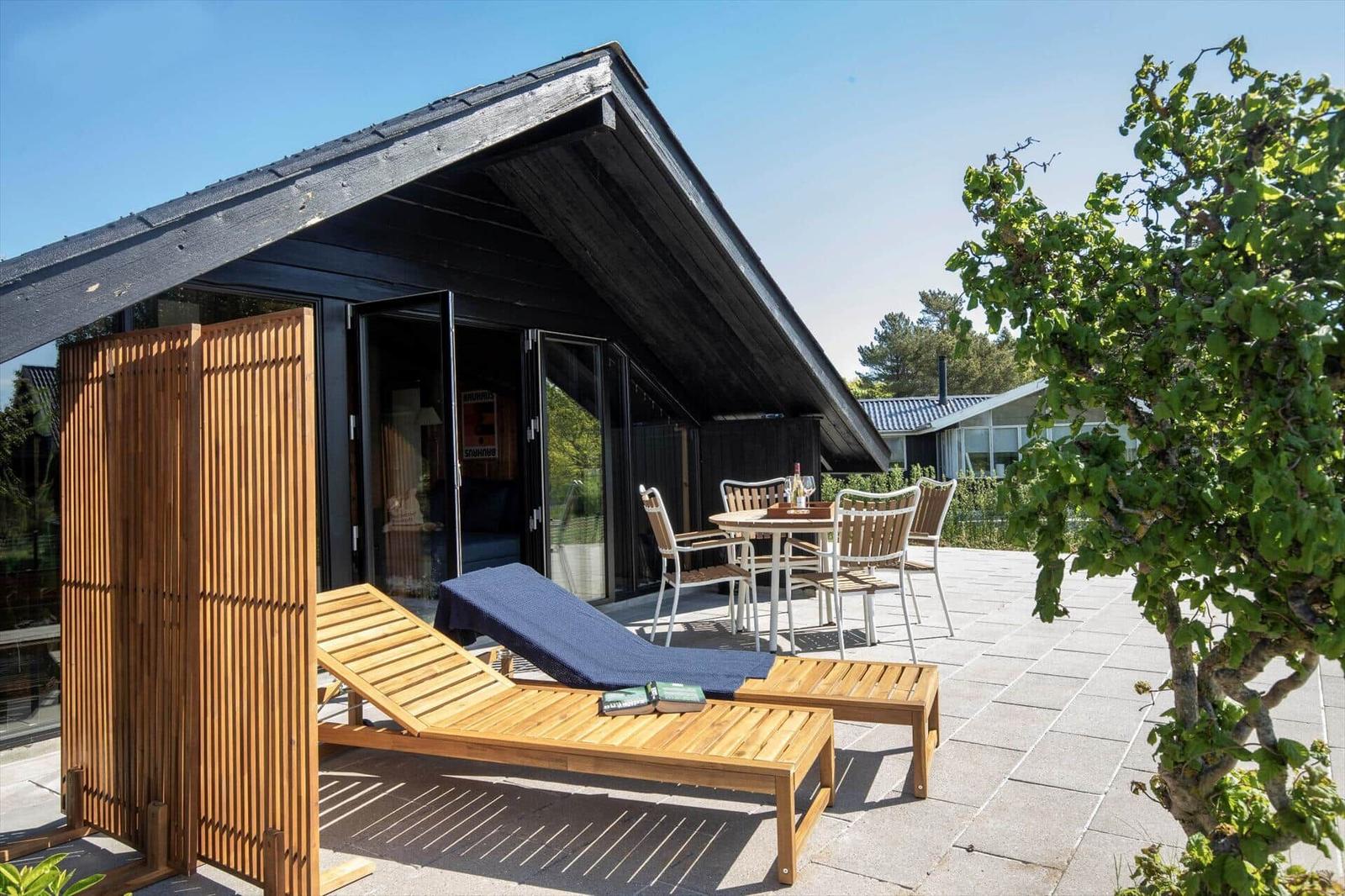 Terrace with lounge chairs, table and chairs in front of a modern house.