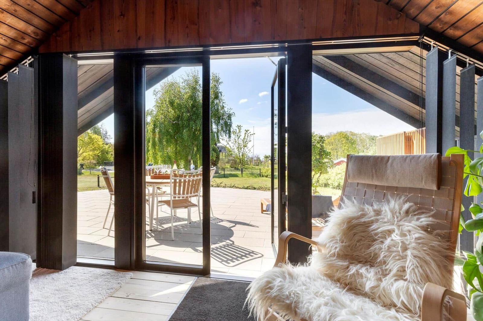 A room with a wooden ceiling and large window view of a terrace with garden.