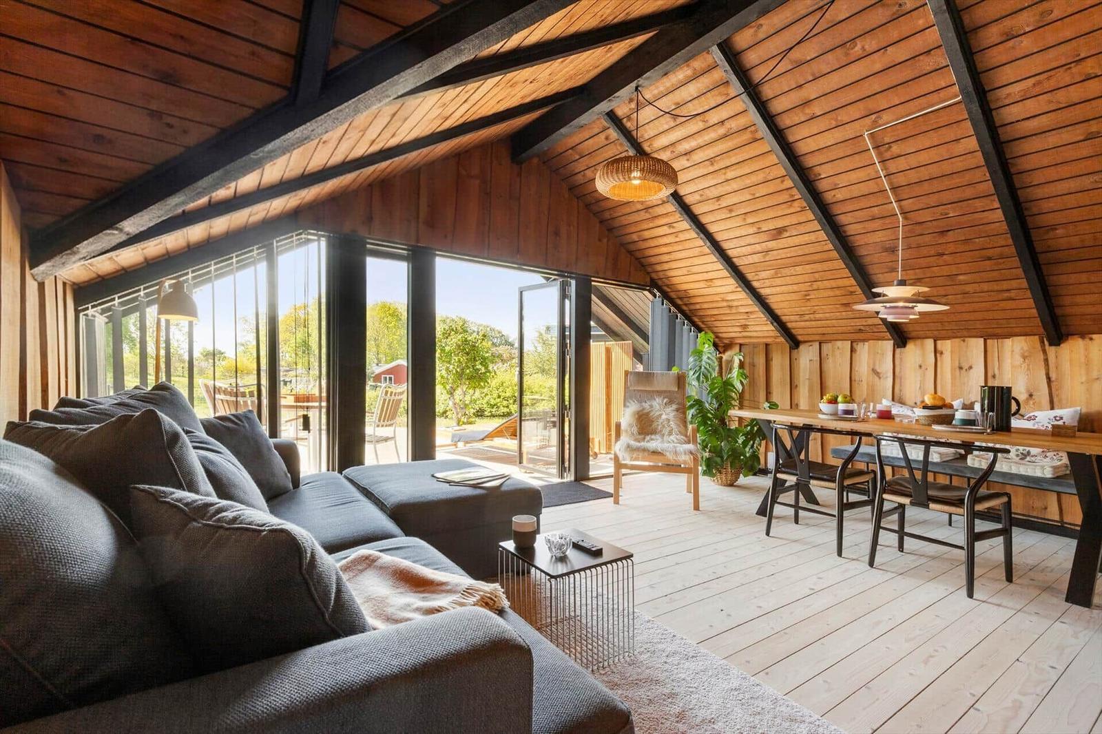 Living and dining area with wooden ceiling, large sofa, and view of the terrace.