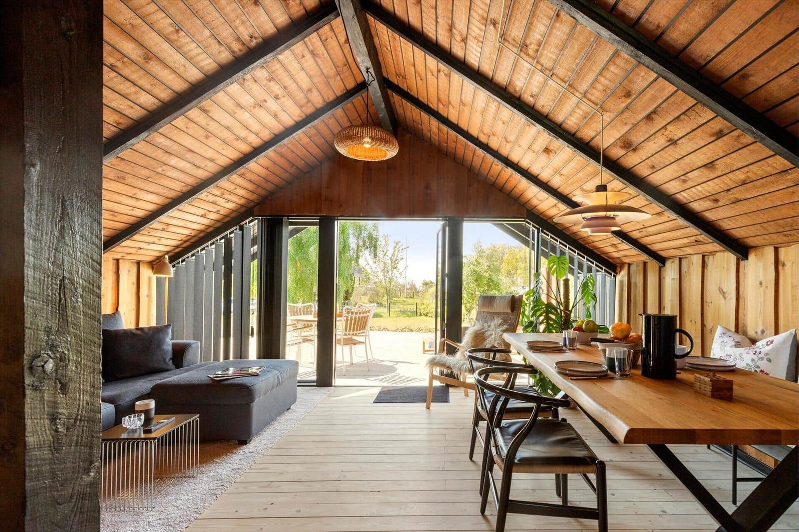 Living and dining area with wooden ceiling, table, and sofa. Passage to terrace with garden view.