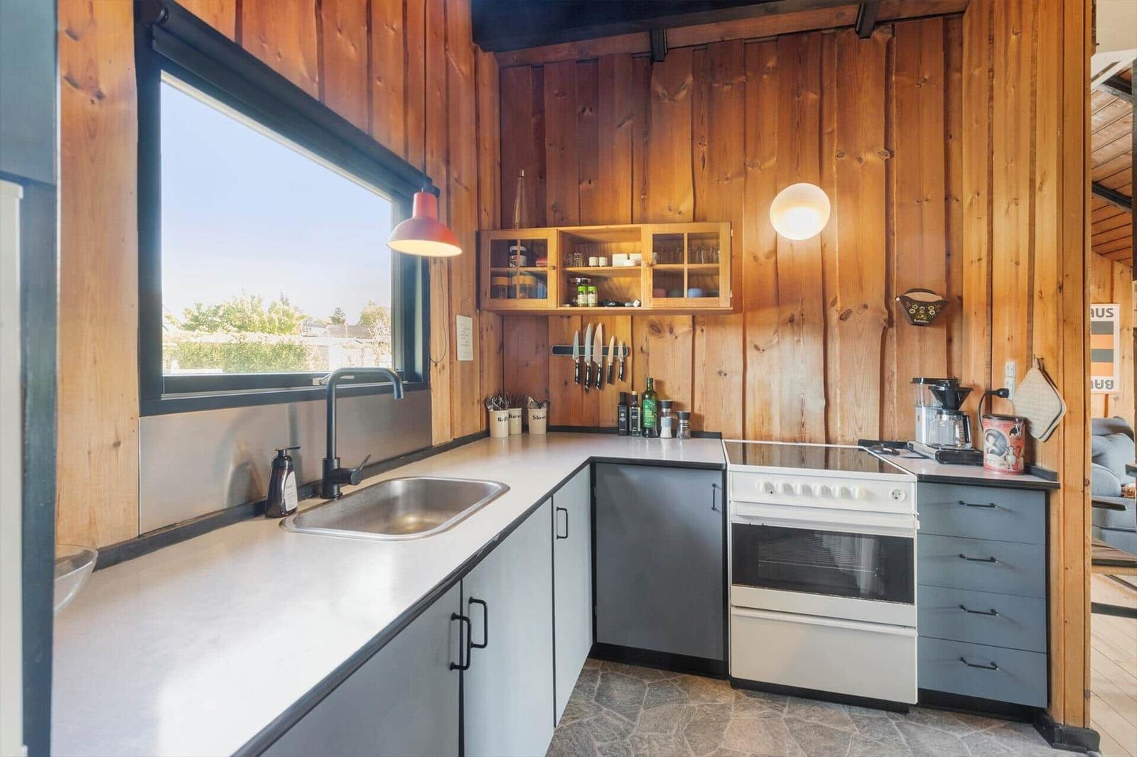 Kitchen with wooden walls, countertop, sink, stove, and window.