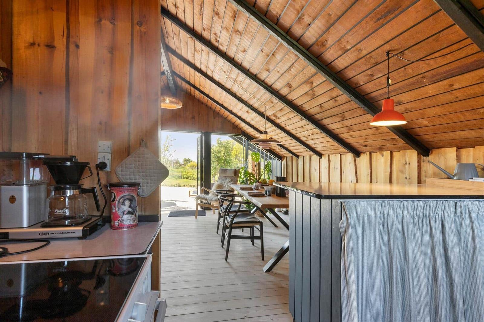 Kitchen with dining area under wooden ceiling, table, chairs, and window view.