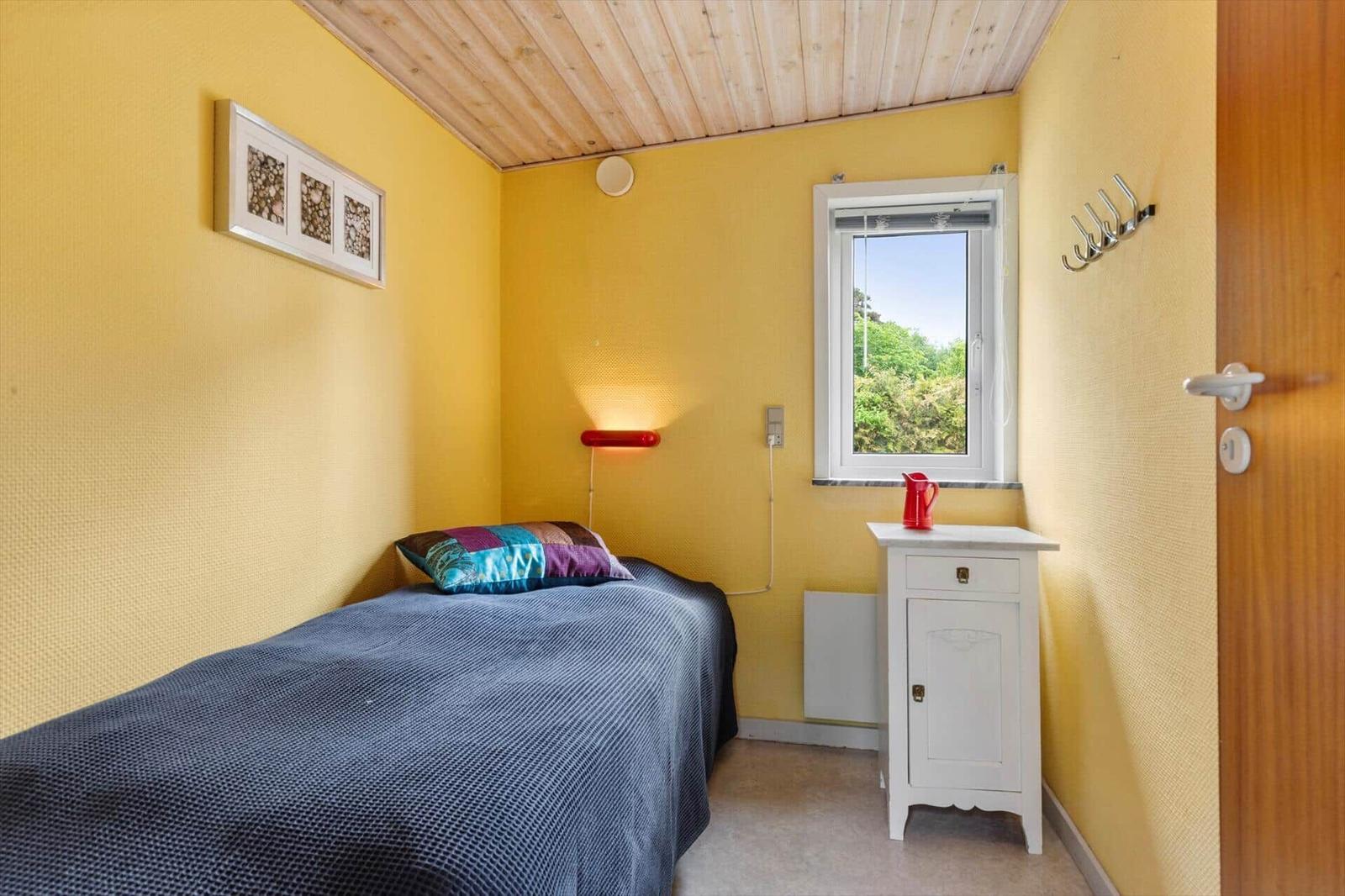 Schlafzimmer mit gelben Wänden, Bett, Fenster und Nachttisch.