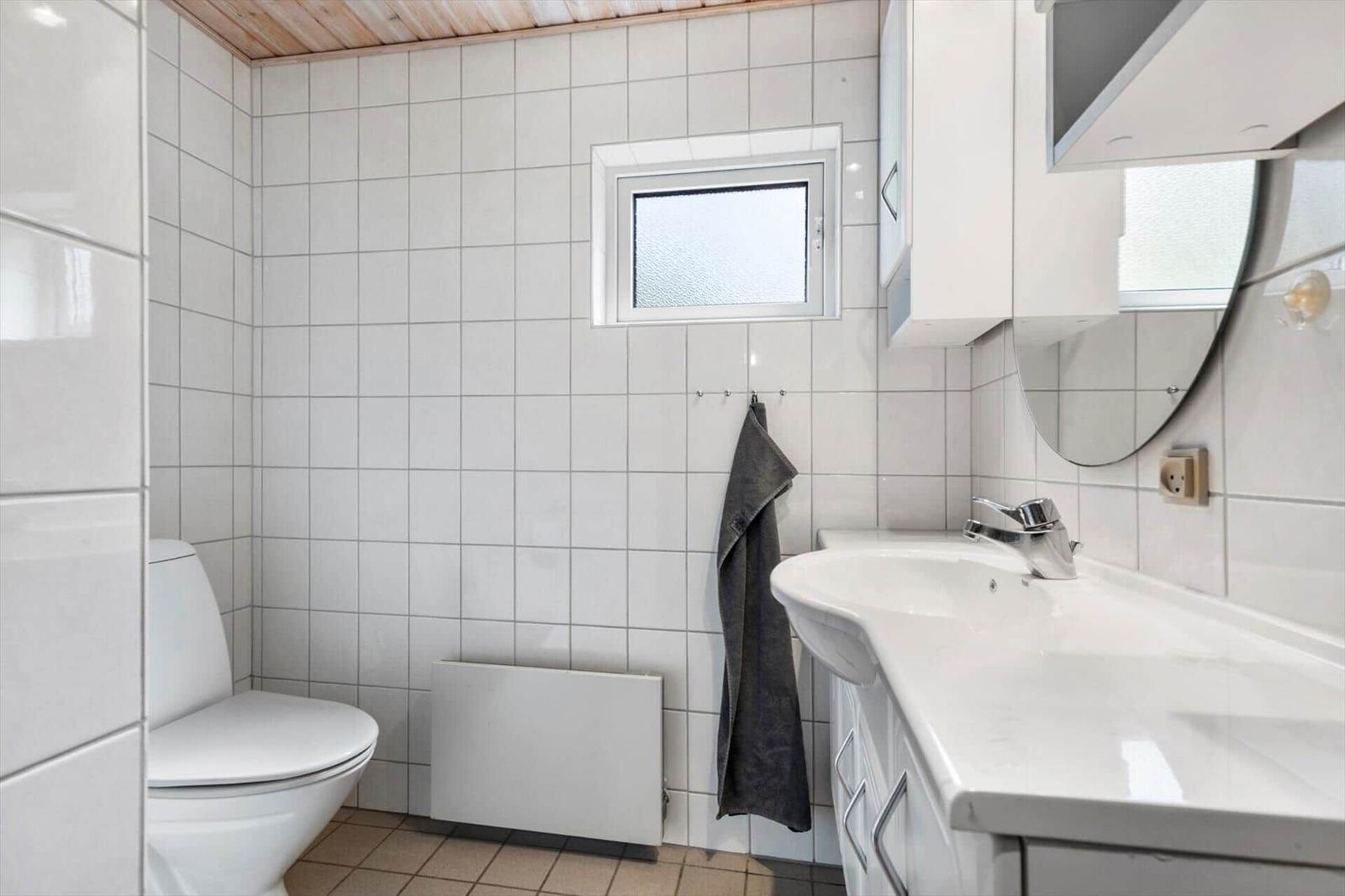 Badezimmer mit Toilette, Waschbecken und Duschbereich mit Fenster.