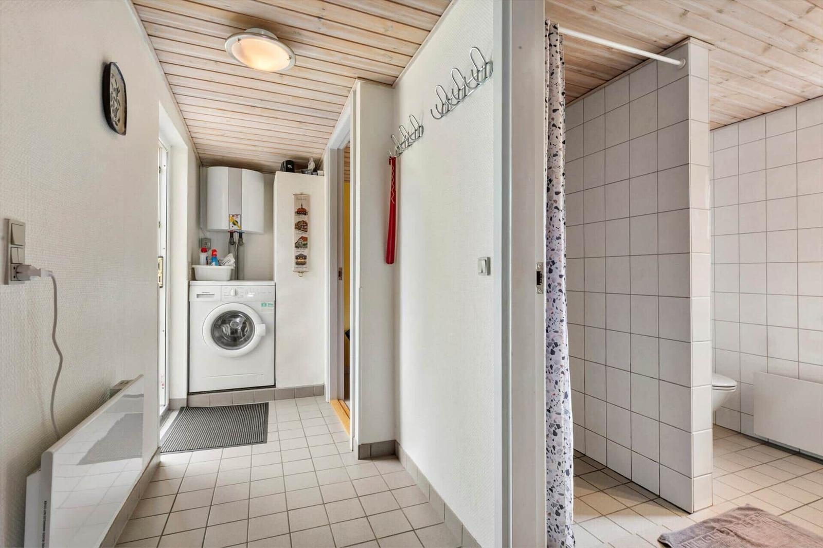 Flur mit Waschmaschine, Dusche und Toilette. Holzdecke und Fliesenboden.