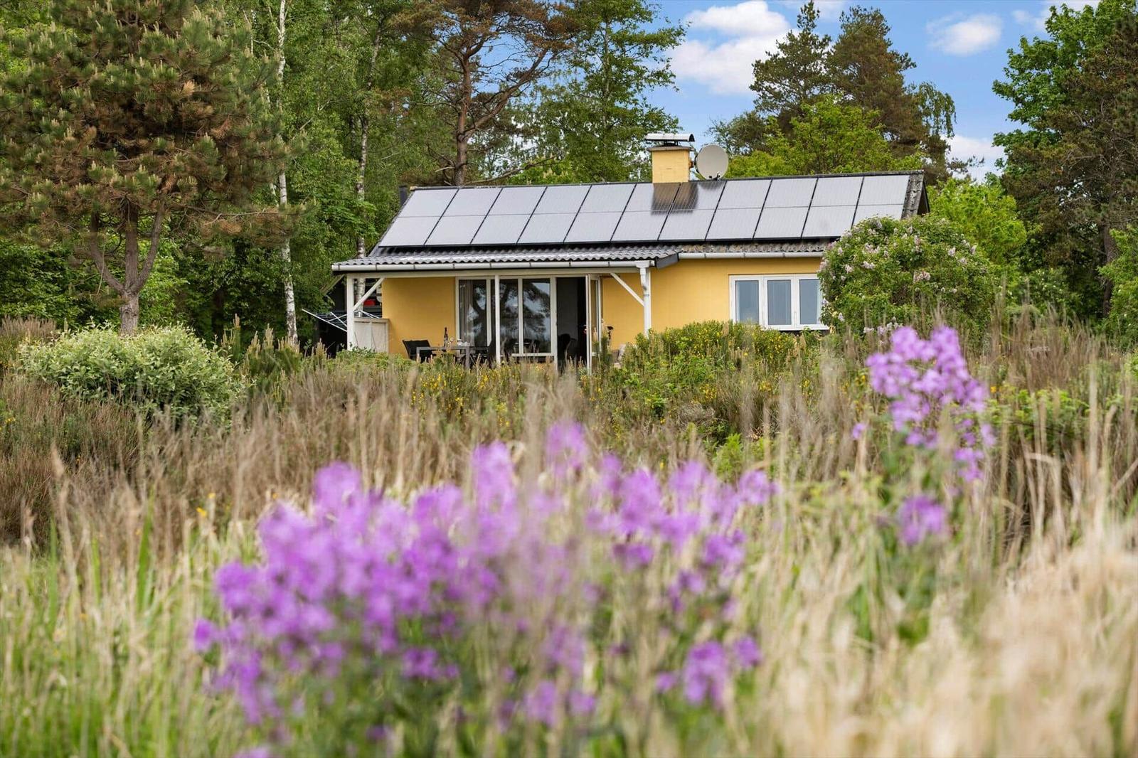 Ein gelbes Haus mit Solaranlage und Balkon im Grünen.