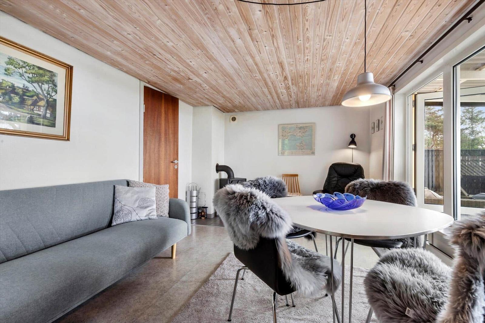 Wohn- und Essbereich mit Holzdecke, Sofa, Tisch und Stühlen mit Fellbezügen.