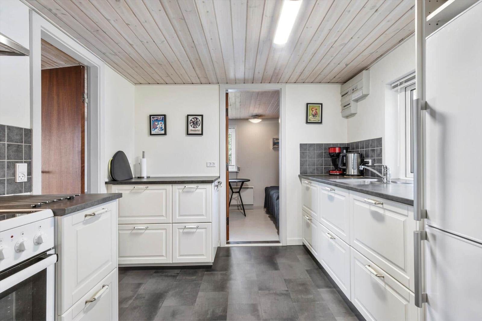Küche mit weißen Schränken, dunklem Boden und Holzdecke. Durchgang zur Schlafzimmer.