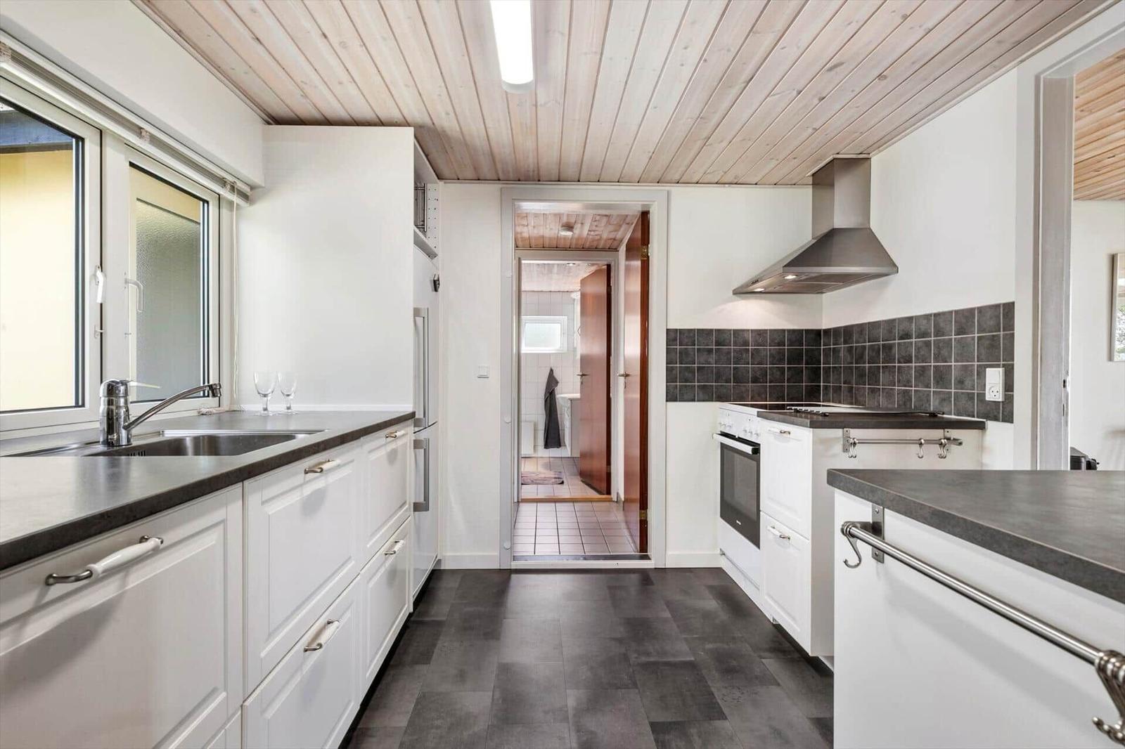 Küche mit weißen Schränken, dunklem Boden und Holzdecke. Blick in das Badezimmer.