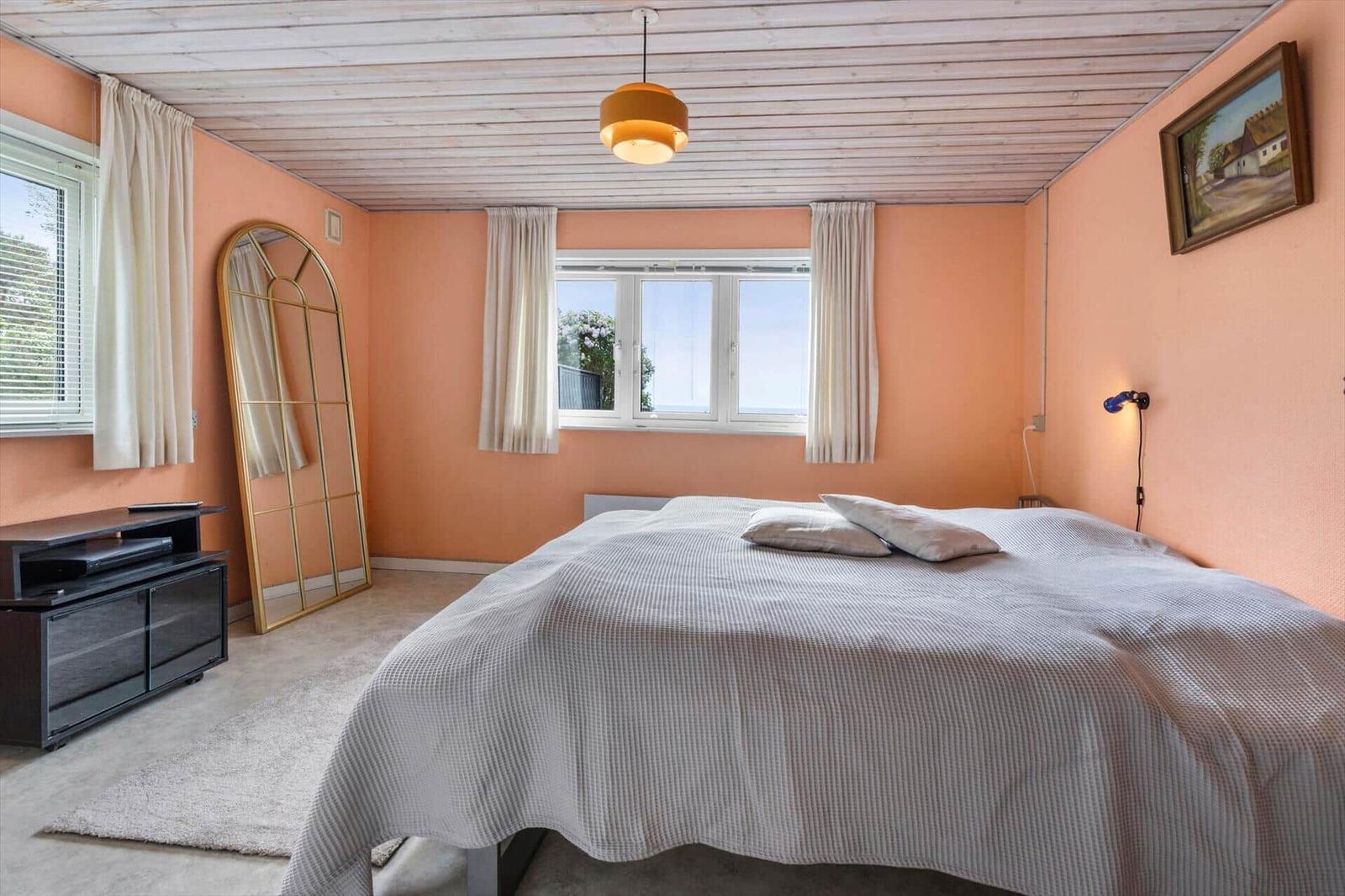 Schlafzimmer mit Bett, Fenster, Spiegel und Deckenleuchte.