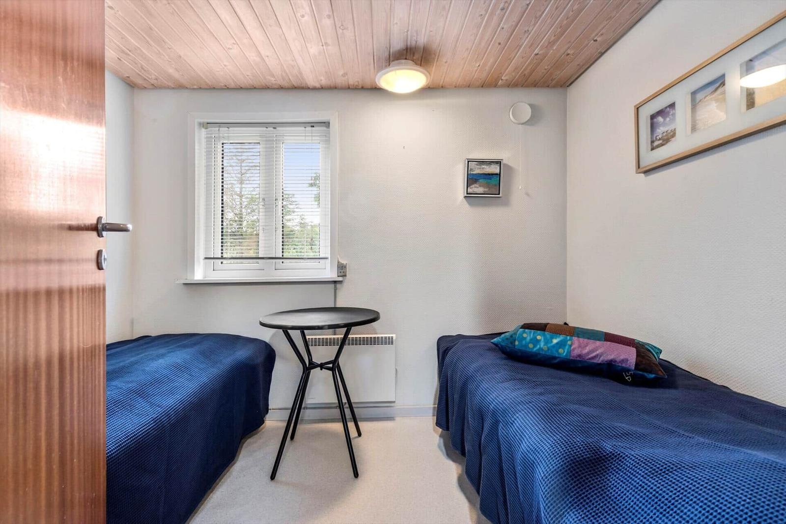 Zimmer mit zwei Betten, Tisch und Fenster mit Jalousie.