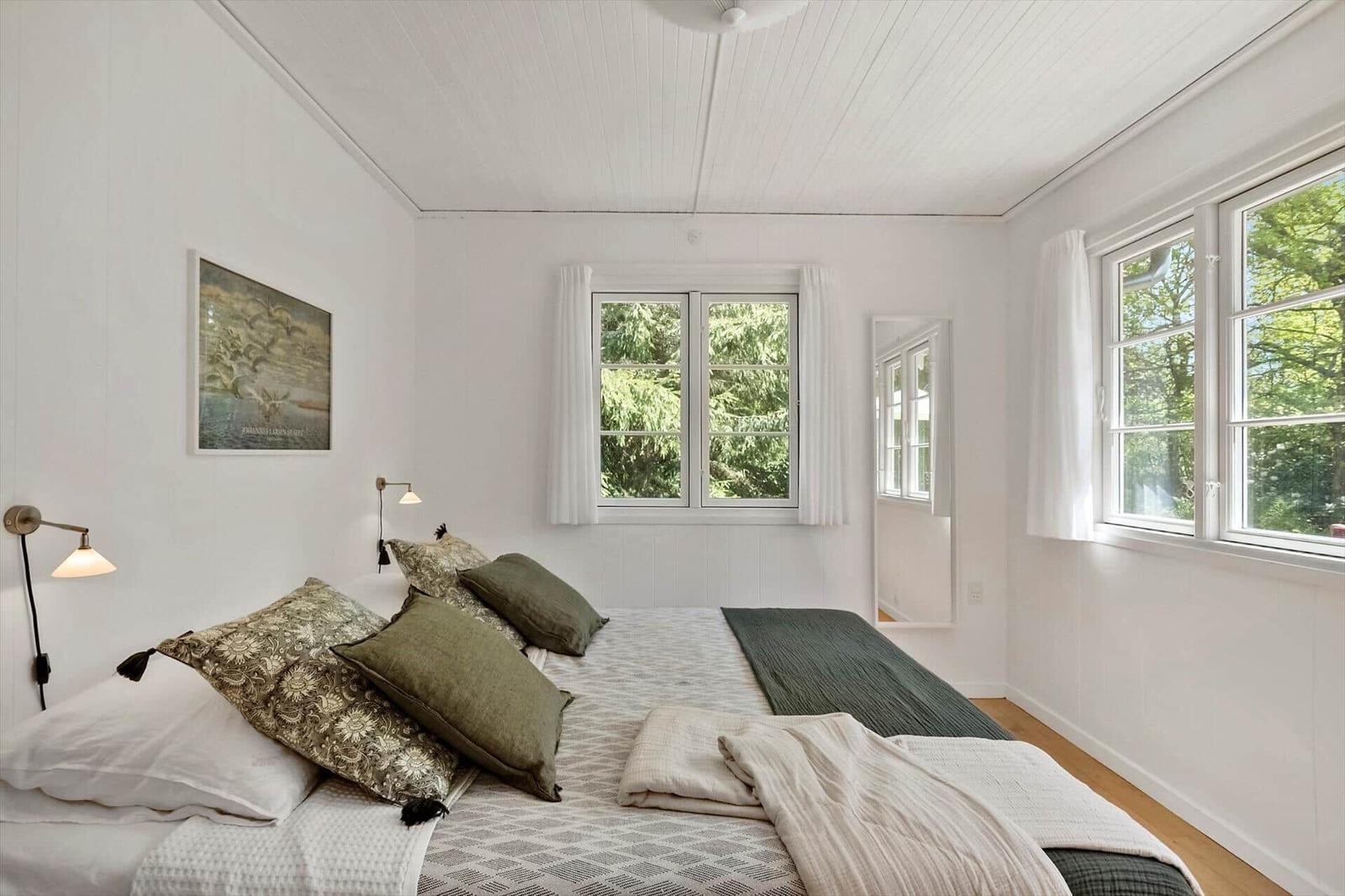 Schlafzimmer mit Bett, Fenstern und Wandbild. Holzdielen und weiße Wände.