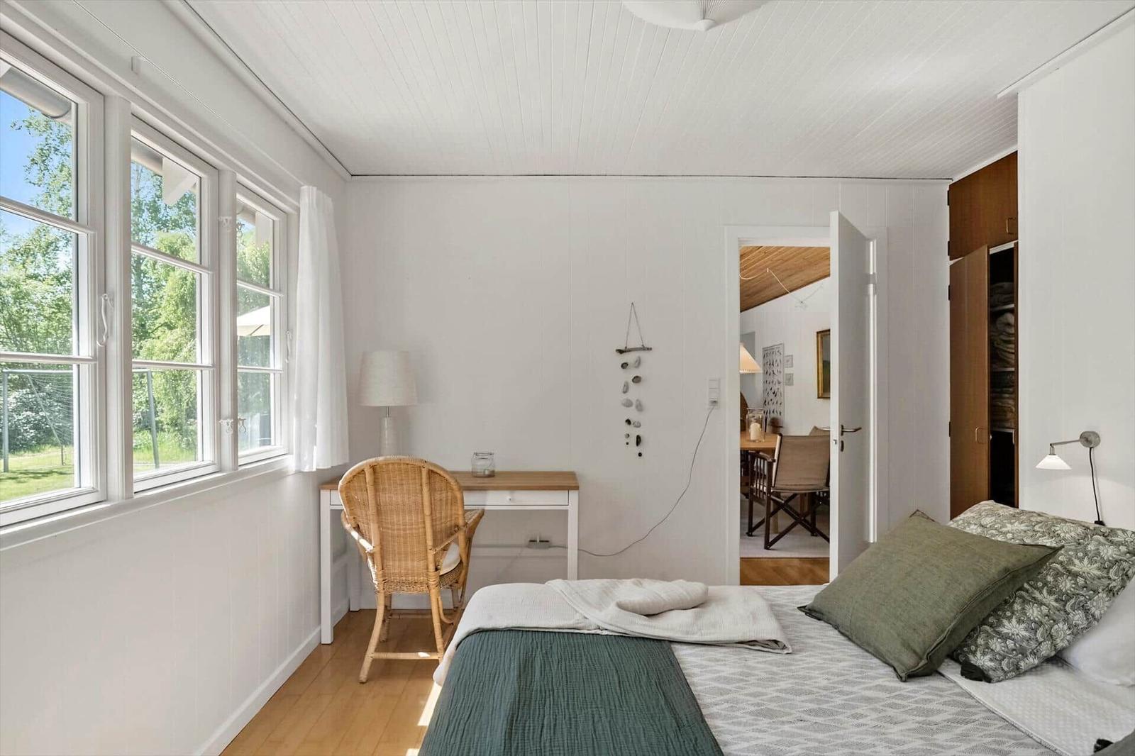 Schlafzimmer mit Bett, Schreibtisch und Fenster. Blick in angrenzenden Raum.