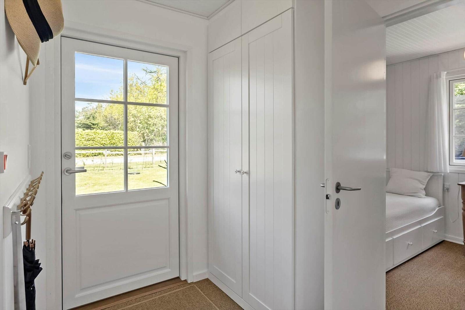 Eingangsbereich mit weißen Schränken und Tür zum Schlafzimmer mit Bett.