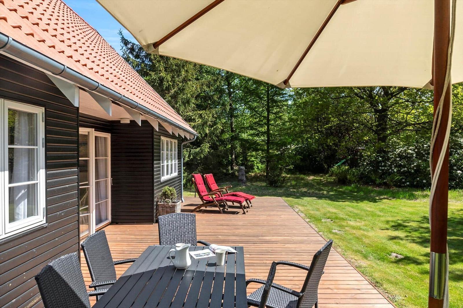 Terrasse mit Tisch, Stühlen und Sonnenschirm neben einem Haus mit Holzfassade.