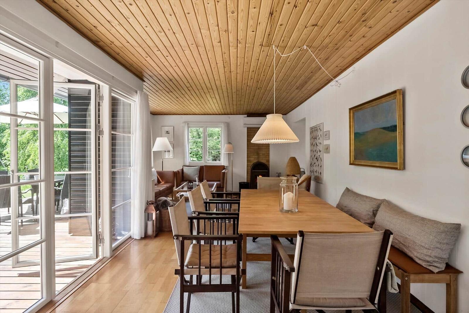 Esszimmer mit Holztisch, Stühlen und Sitzbank. Holzdecke und große Glastüren zu Terrasse.