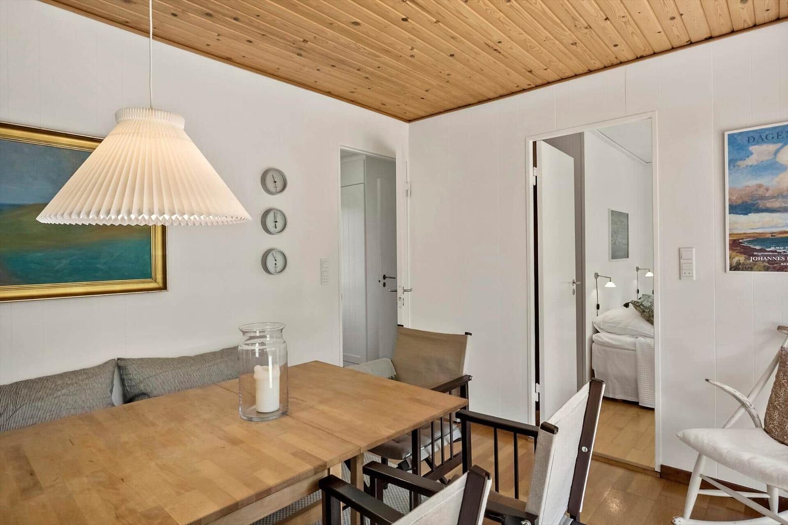 Essbereich mit Tisch, Stühlen und Deckenleuchte. Durchgang zu Schlafzimmer mit Bett.