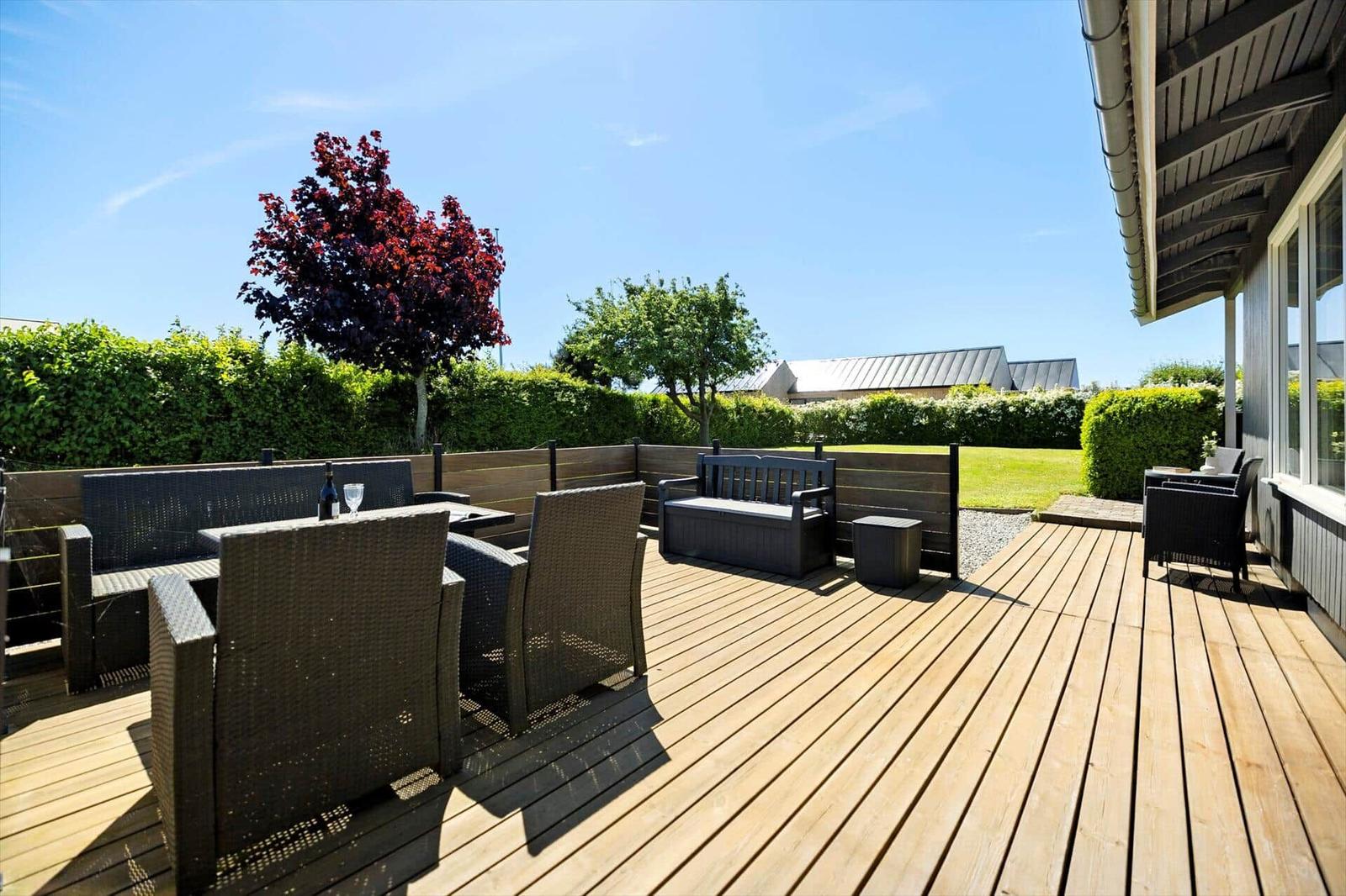 Wooden terrace with garden furniture, bench, and view of green lawn.