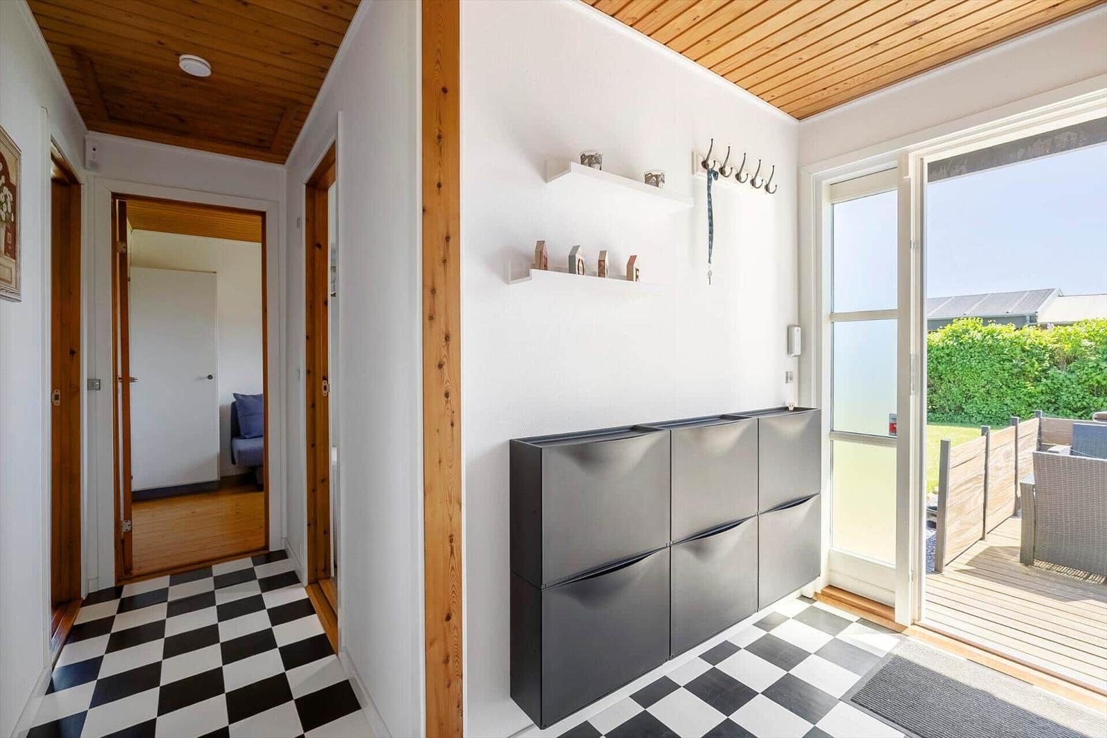 Entryway with black-and-white floor and shoe cabinet. Corridor to bedroom. Terrace with garden view.