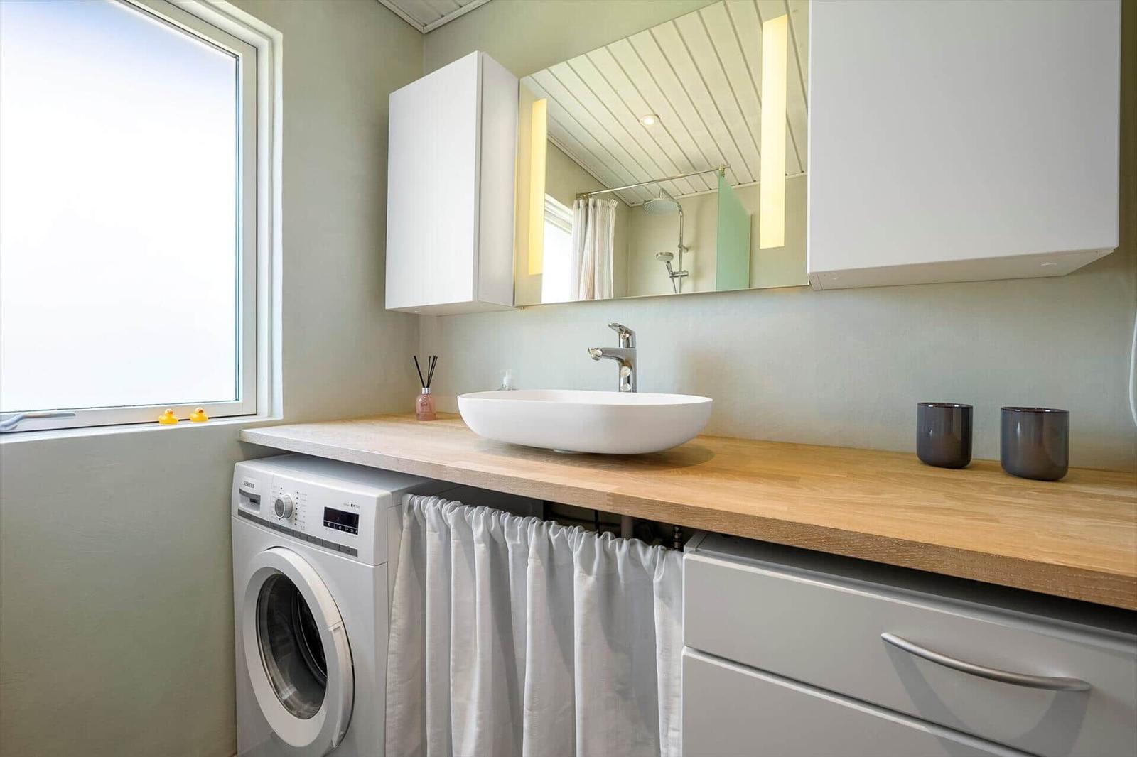 Bathroom with washing machine, sink, and mirror. Window with two rubber ducks.