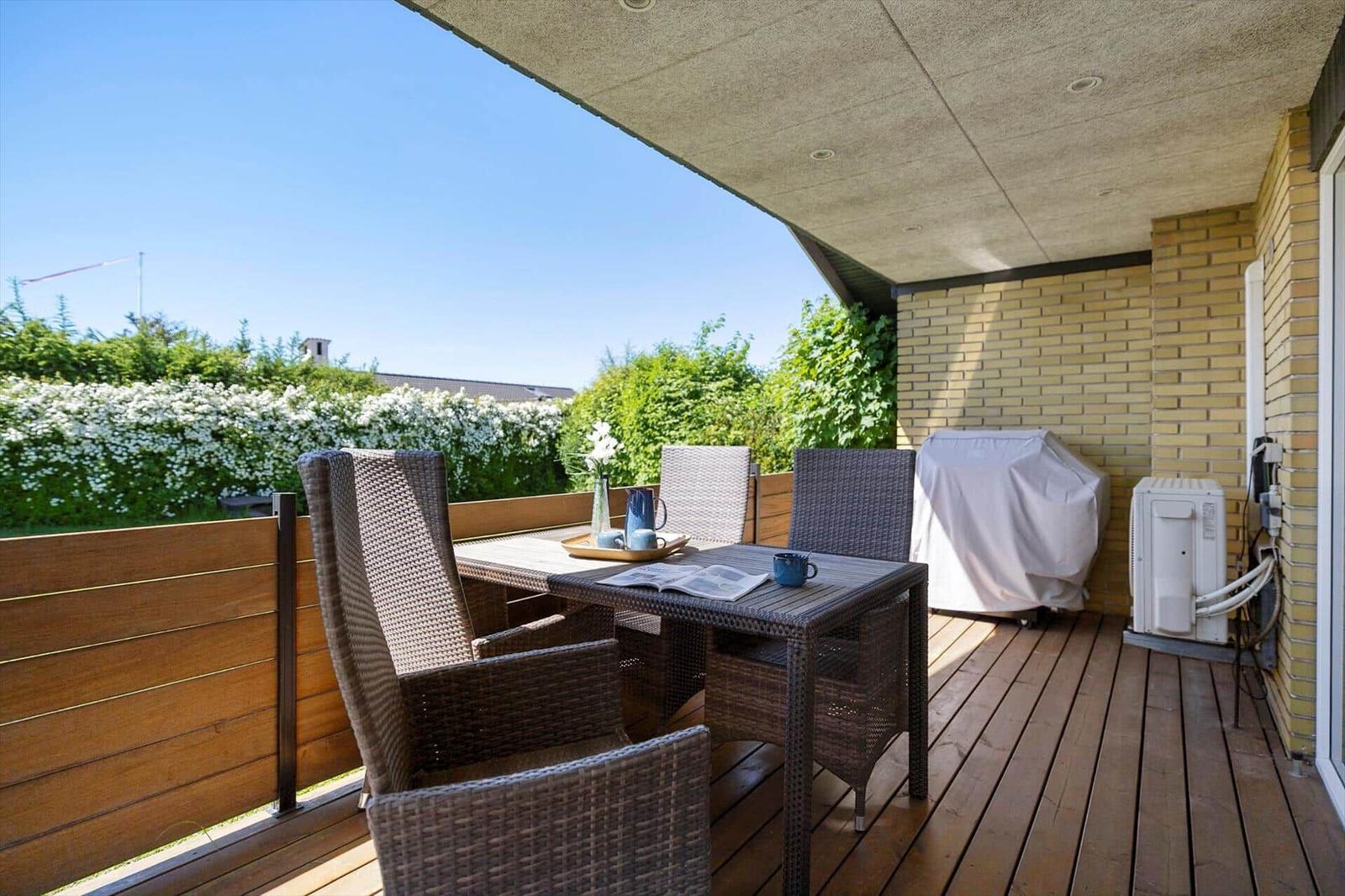 Terrace with garden furniture, table, and view of green hedge.