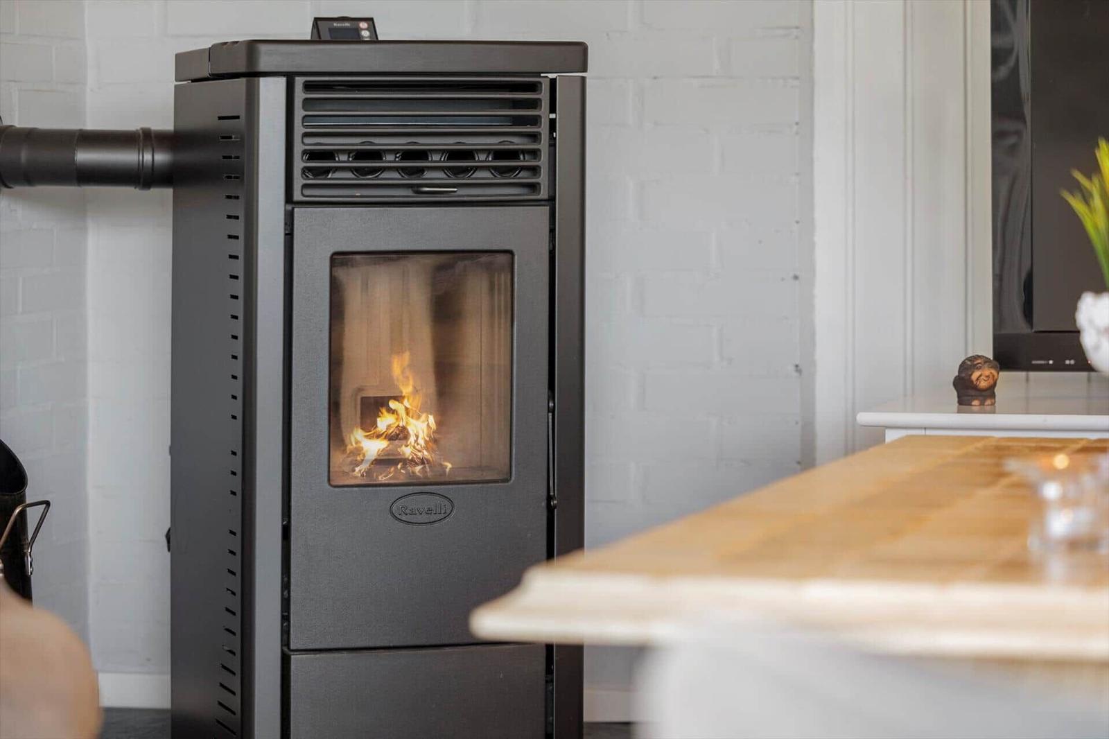 Ravelli wood stove with burning fire in modern kitchen with white brick wall.