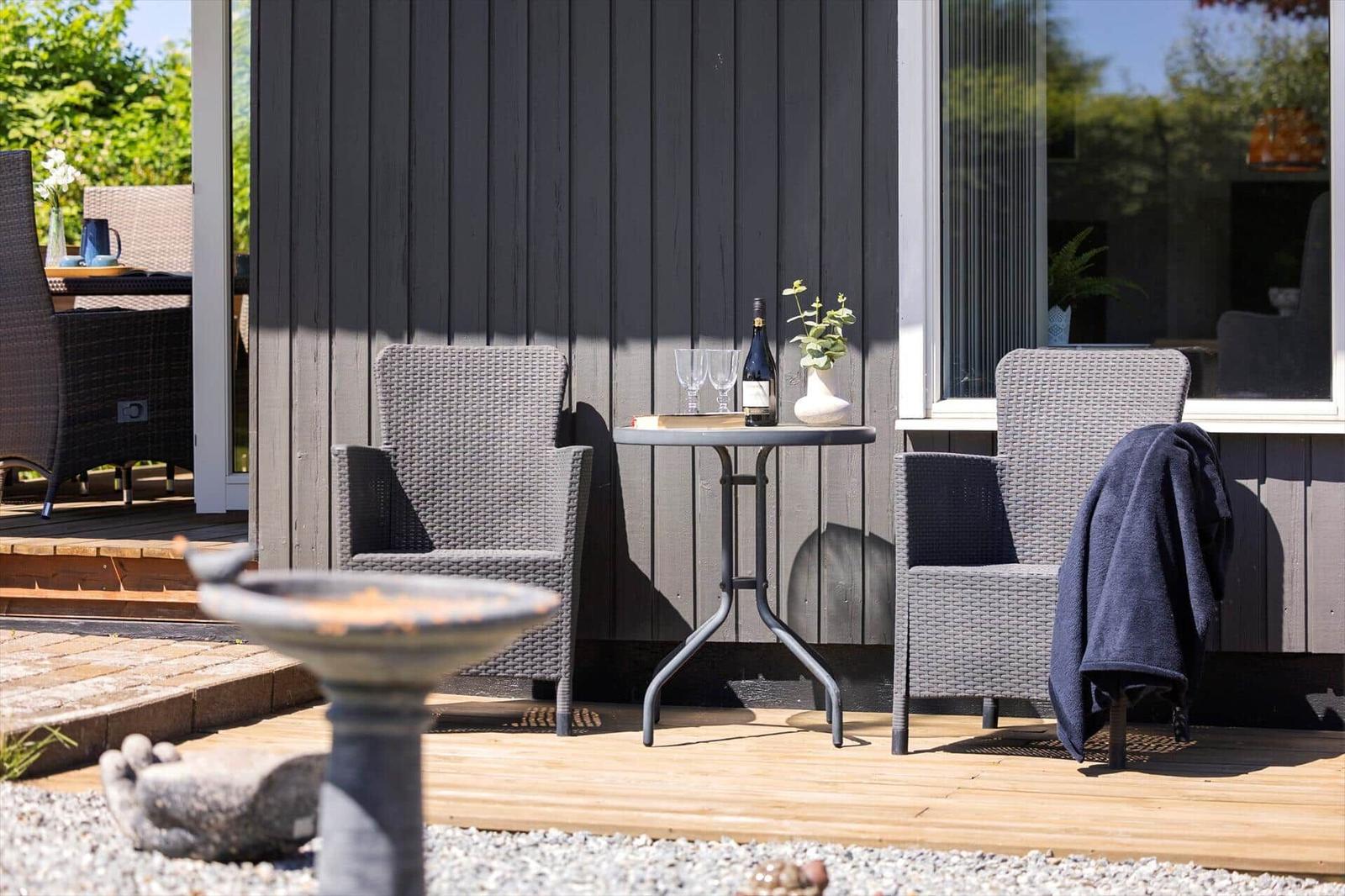 Outdoor area with two chairs, table, and wine bottle against gray siding.