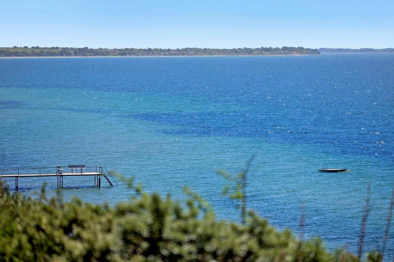 Sea view with pier and small boat in the water. Holiday home directly on the shore.
